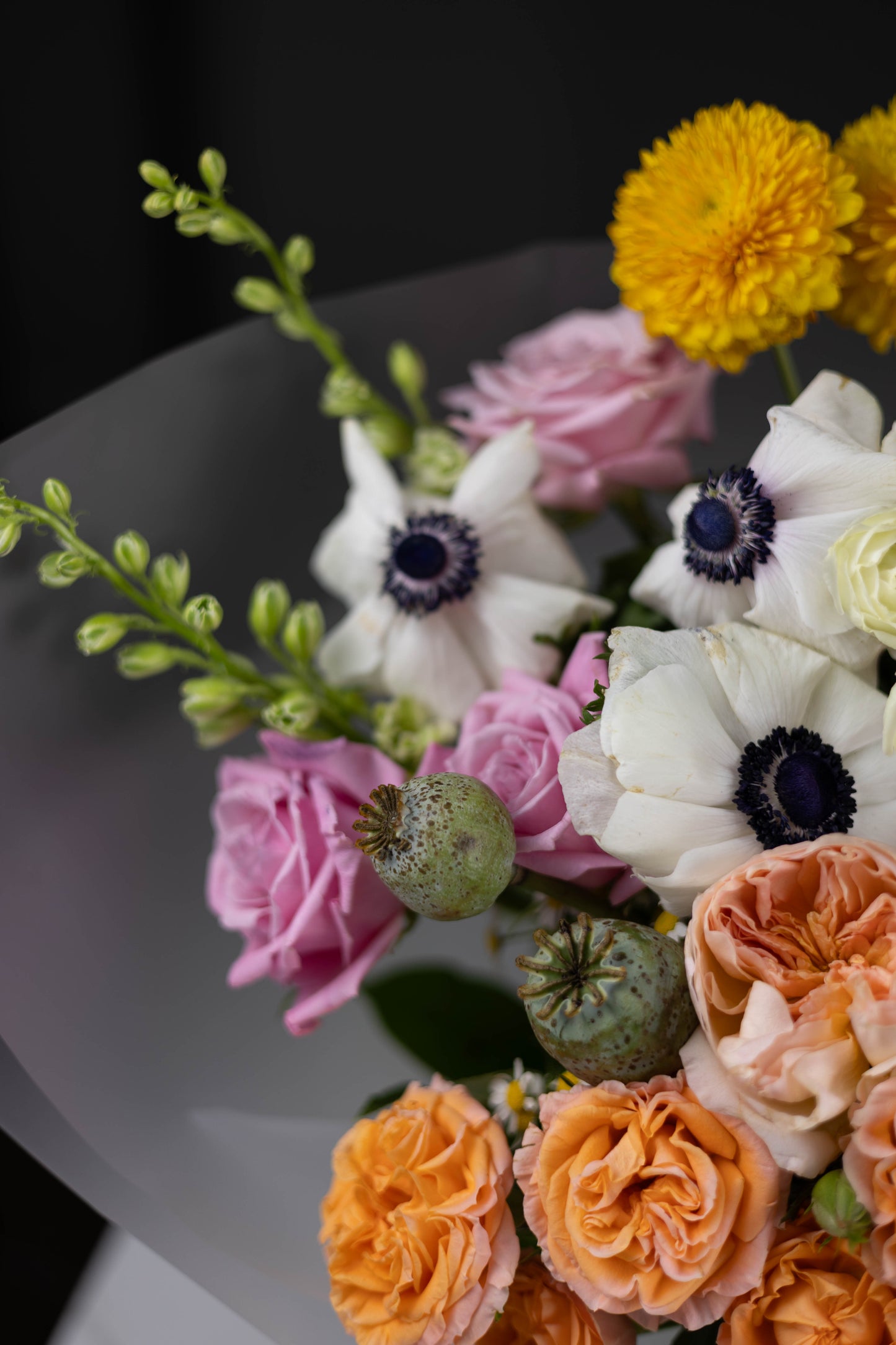 Close-up of a bouquet with orange garden roses, white anemones, pink roses, and poppy pods