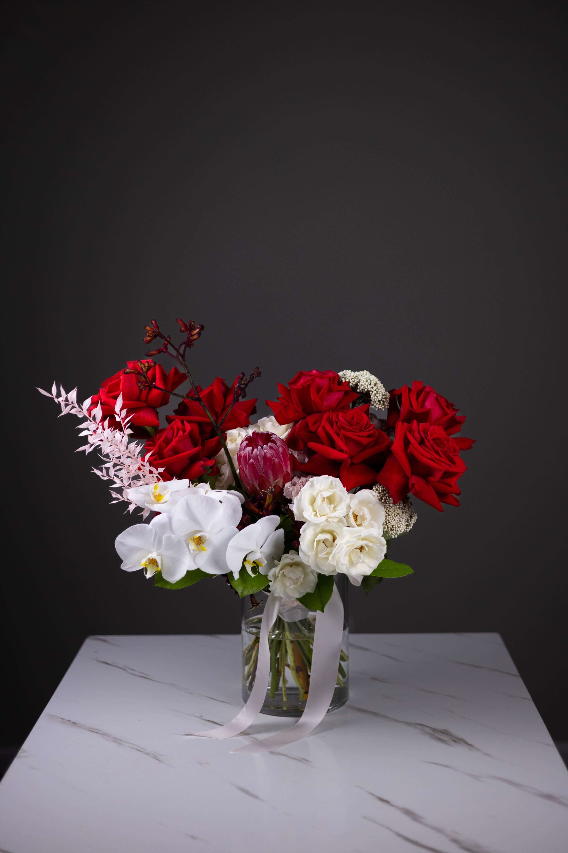 Bouquet of red and white flowers in a clear vase on a dark background