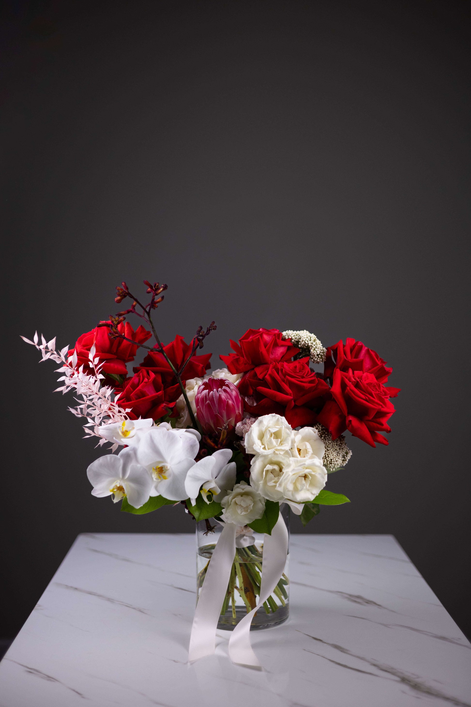 Bouquet of red and white flowers in a clear vase on a gray surface with a dark background