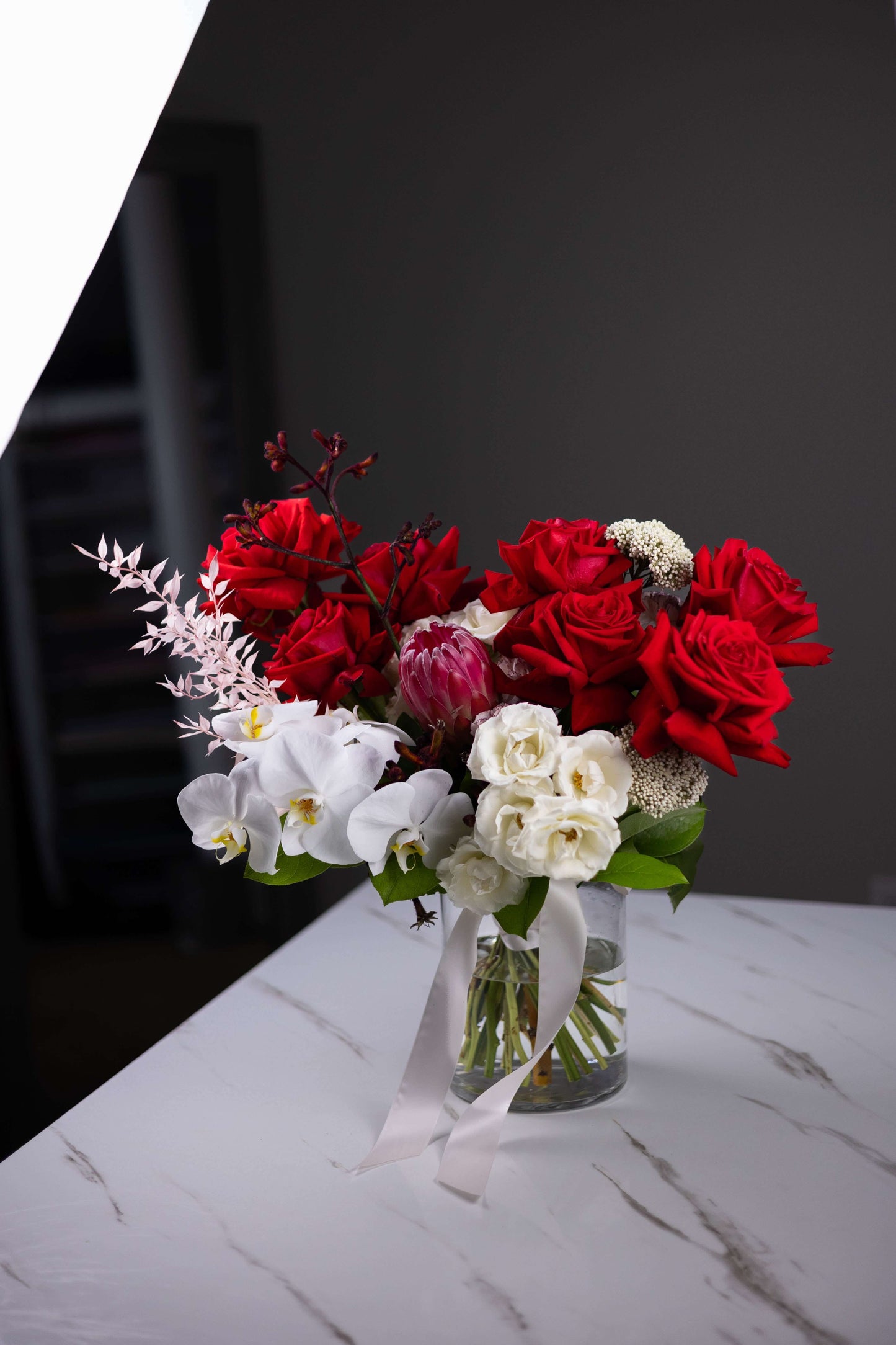 Bouquet of red and white flowers in a clear vase on a marble surface with a dark background