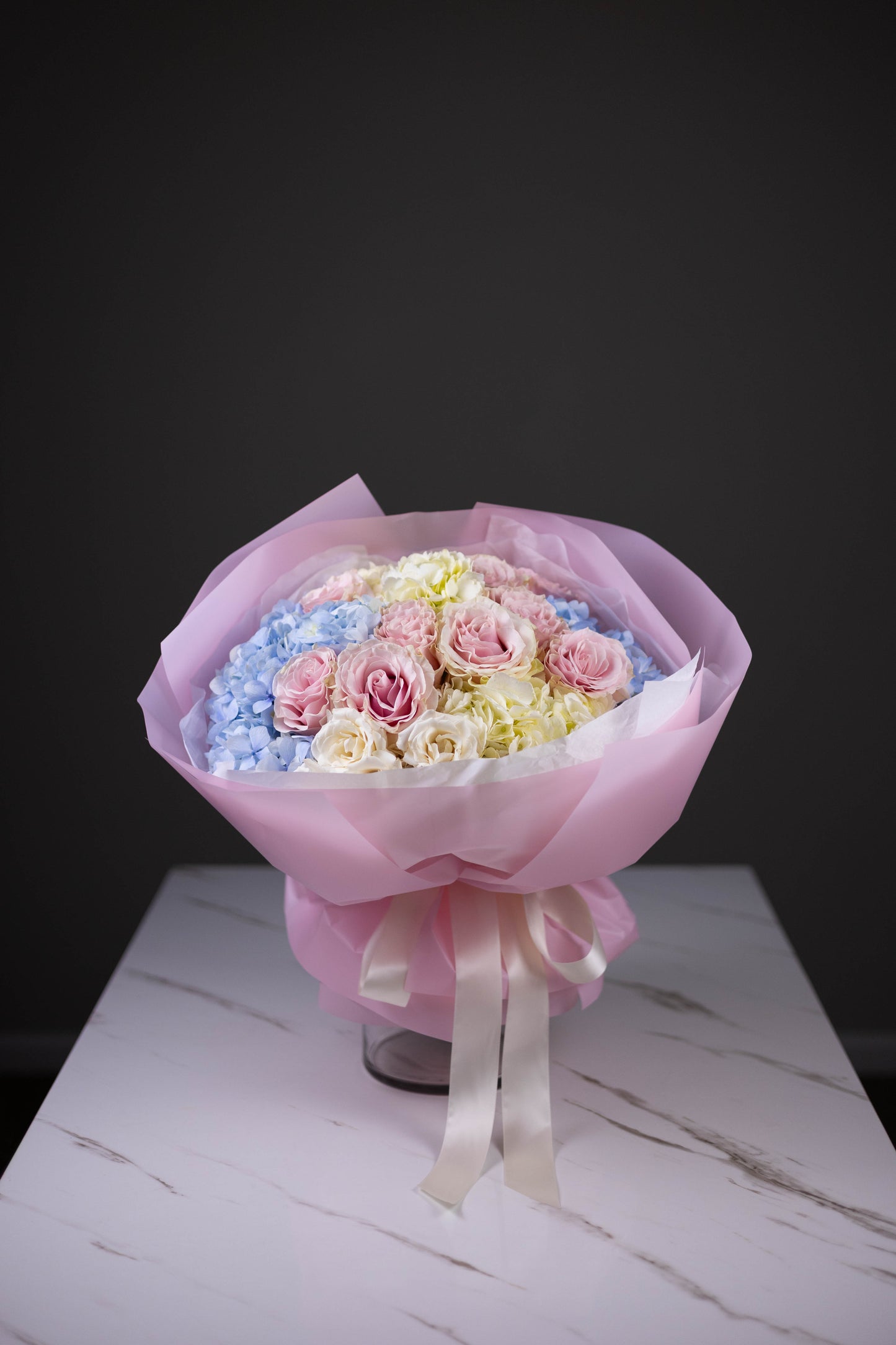 Bouquet of flowers wrapped in pink paper with a ribbon on a white surface.