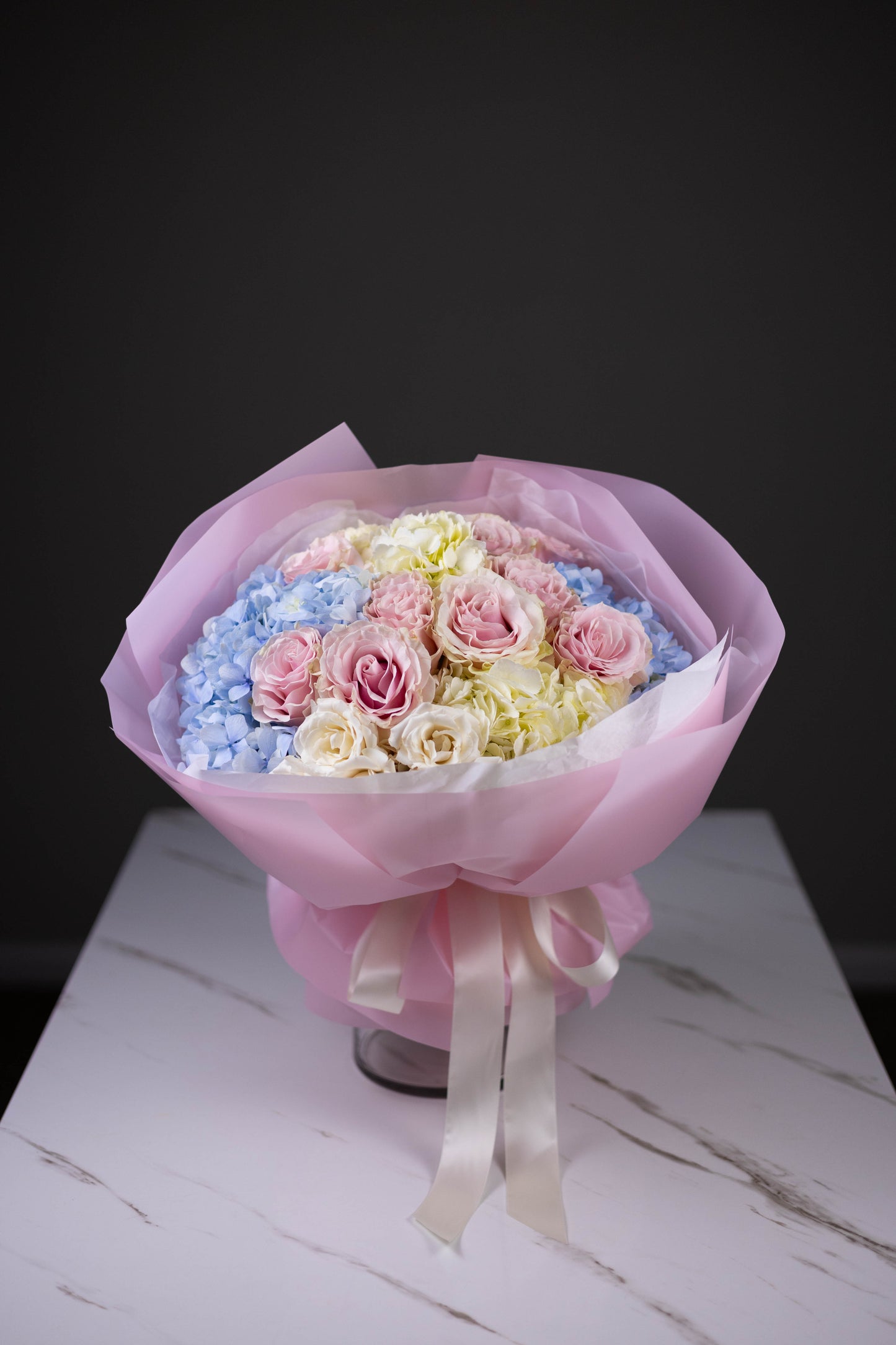 Bouquet of pastel-colored roses in a pink wrap on a white surface with a dark background