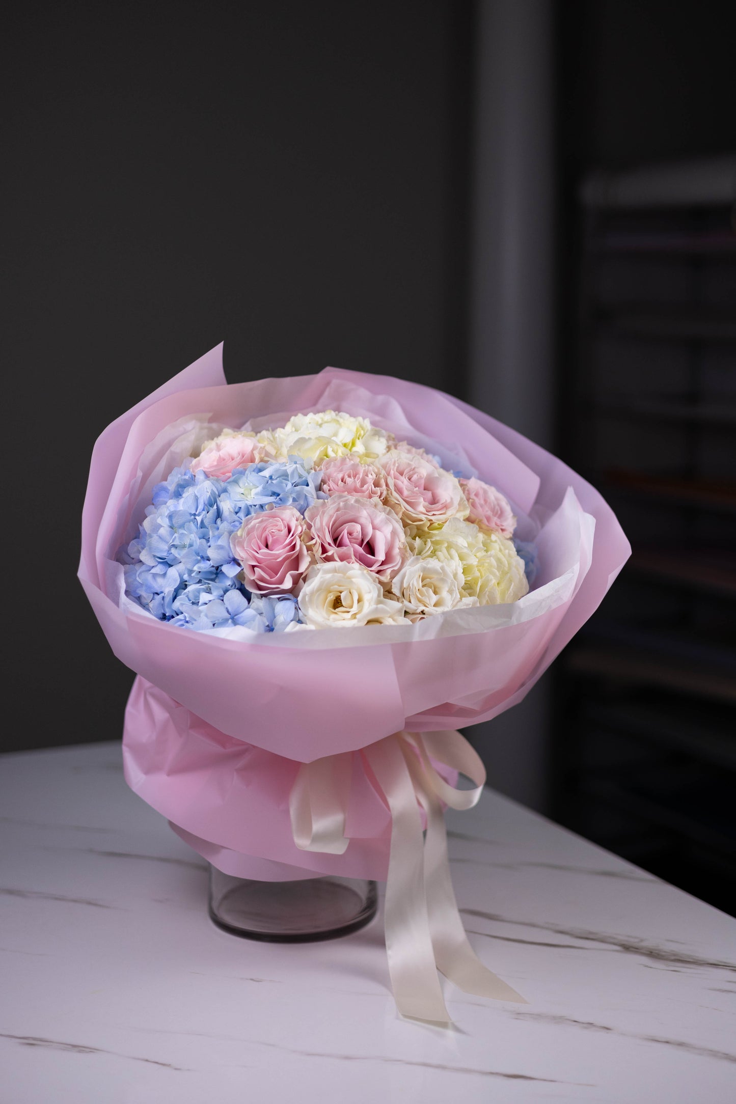 Bouquet of flowers wrapped in pink paper with a ribbon on a white surface.