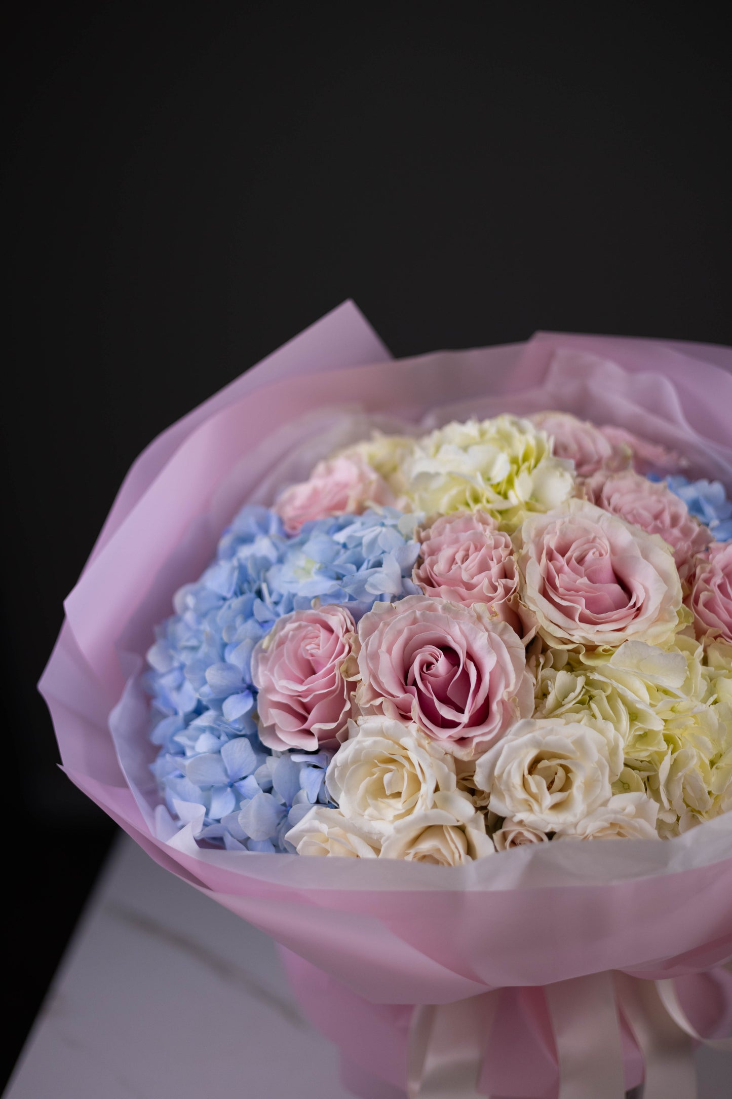 Close-up of pastel rose and hydrangea bouquet in pink wrap with soft satin ribbon