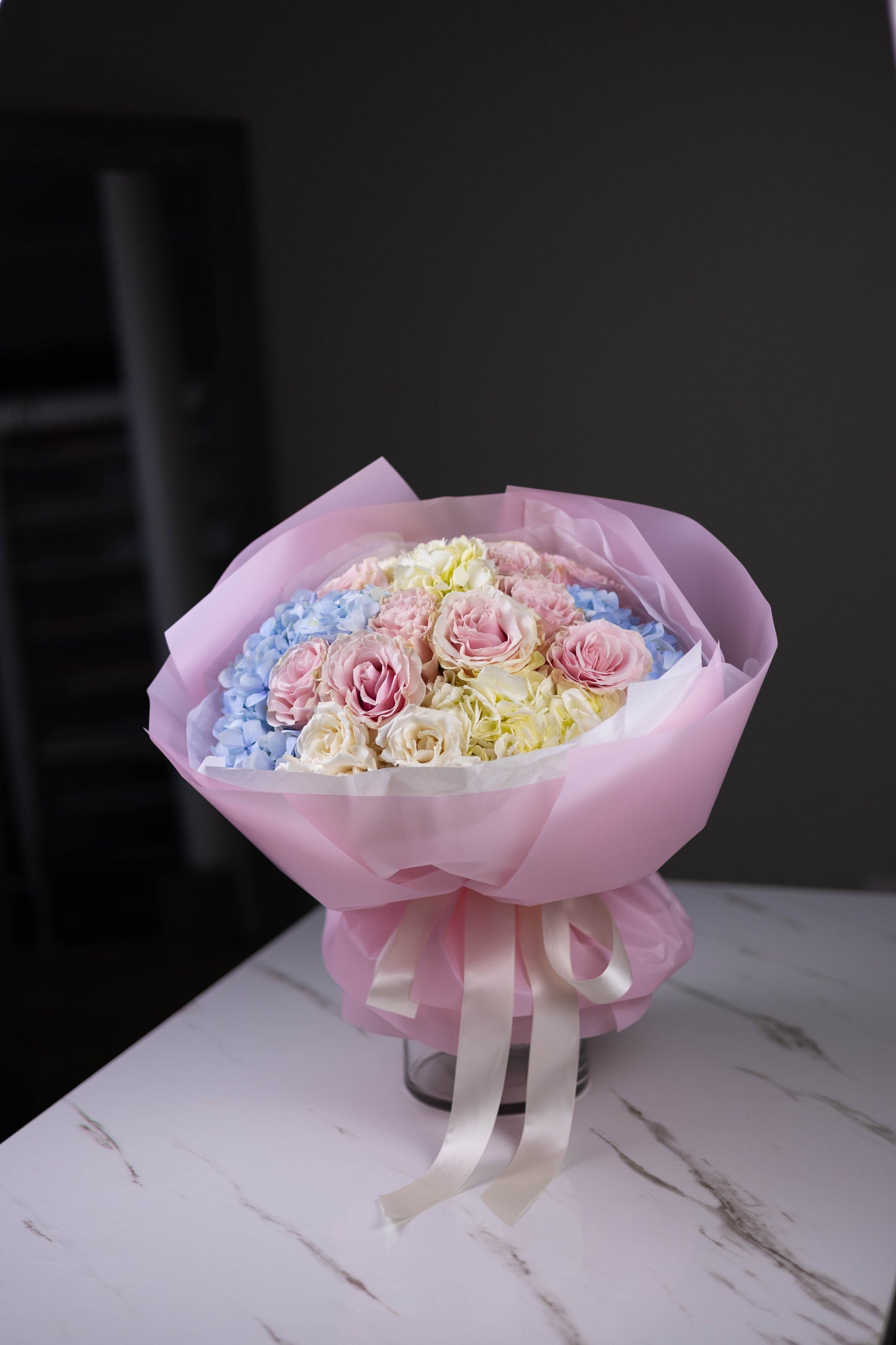 Bouquet of flowers wrapped in pink paper with a black background