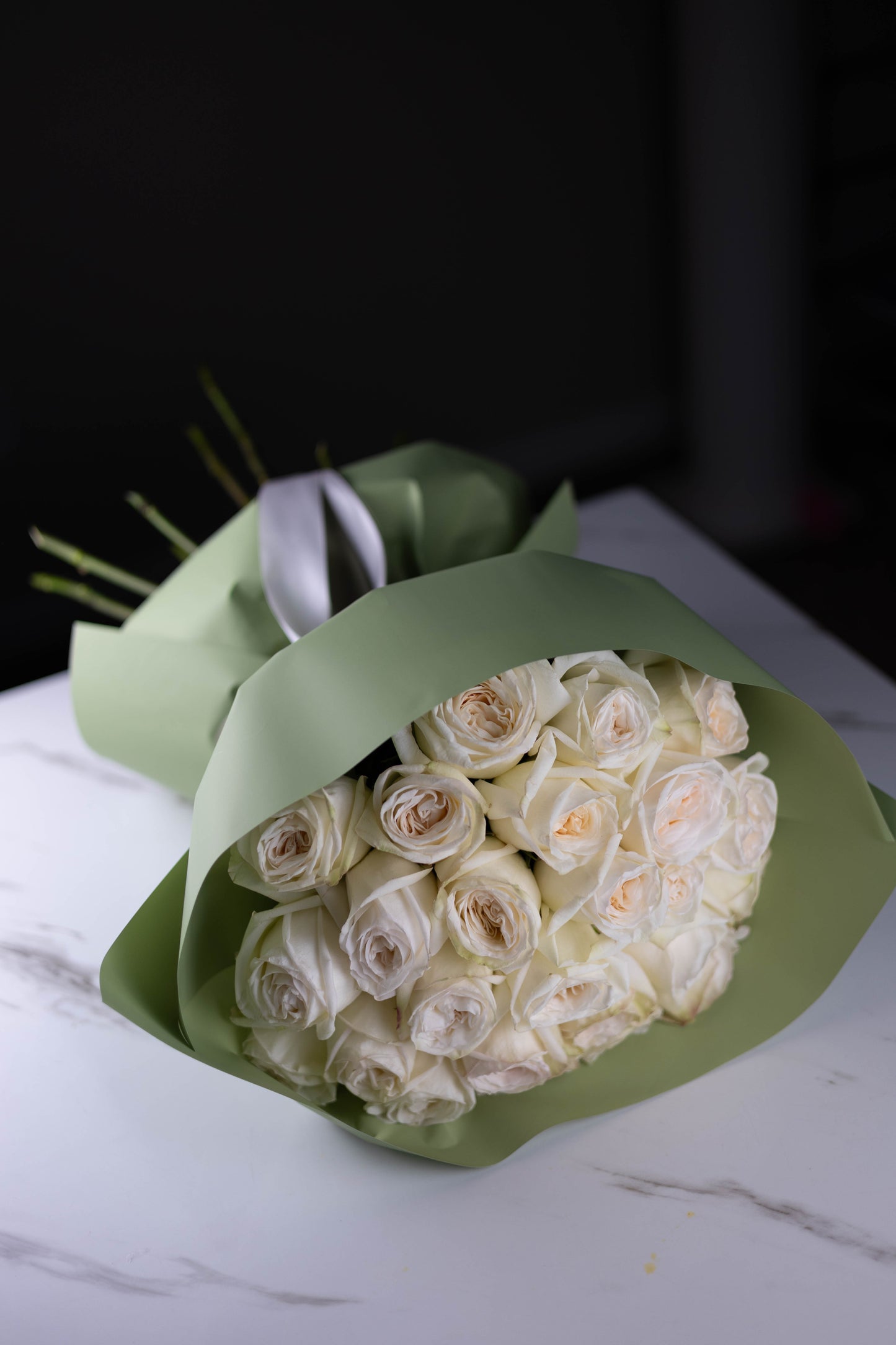 Top view of a bouquet of premium white roses with blush centers, wrapped in minimalist sage-green paper.