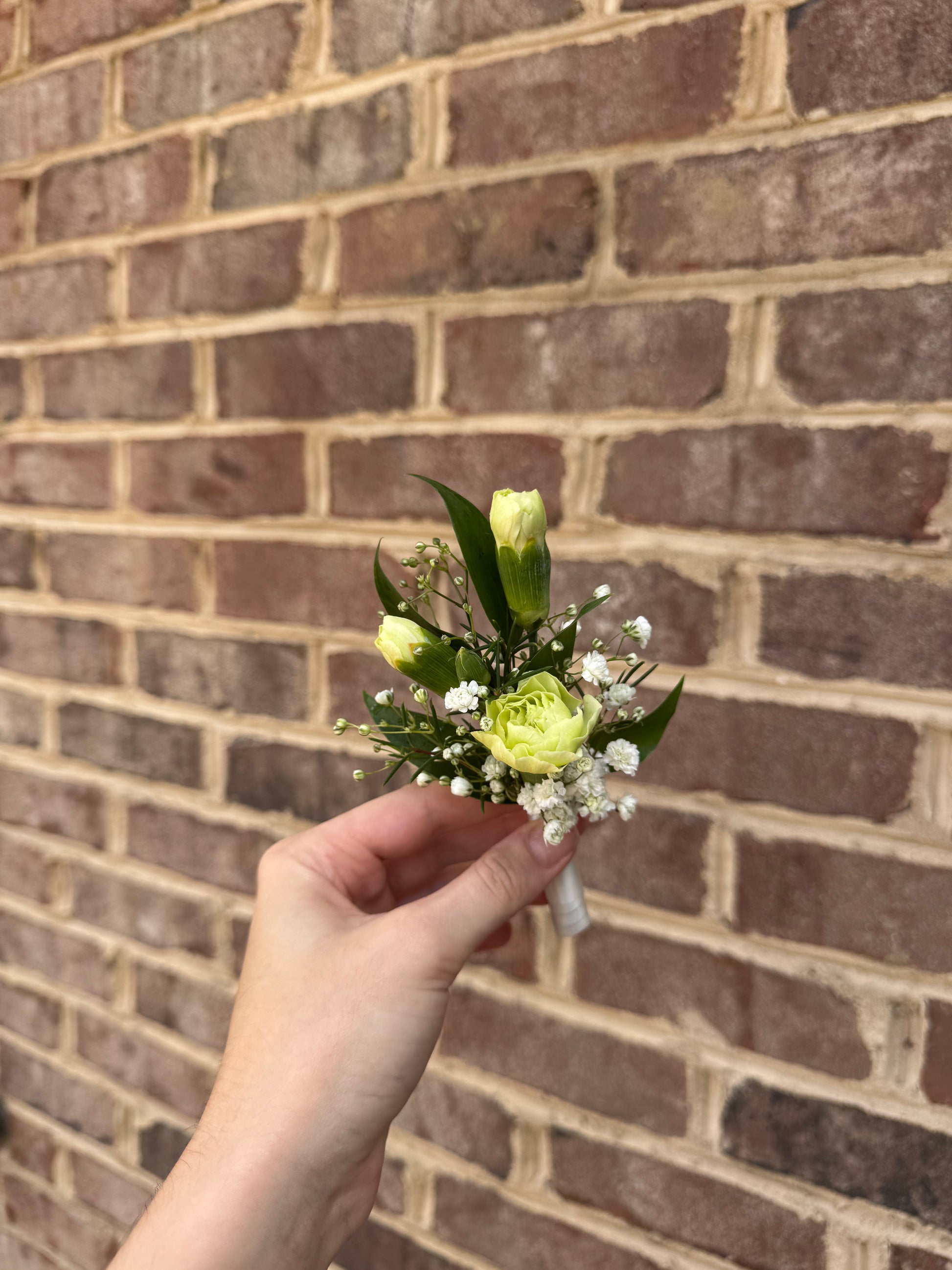 Hand holding a boutonniere against a brick wall