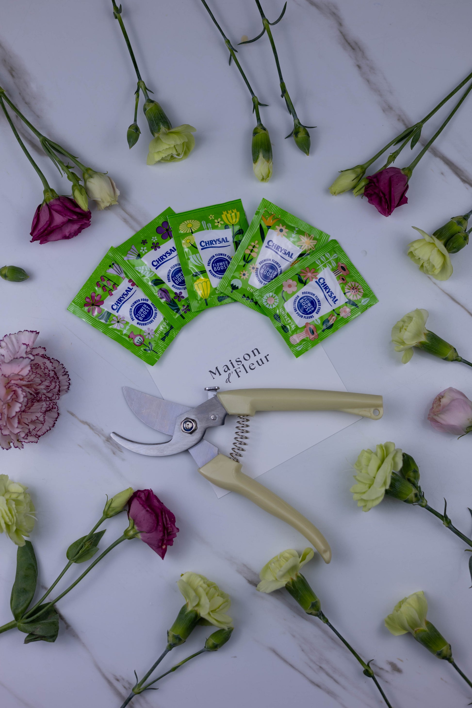 Floral pruners and packets on a marble surface with flowers scattered around