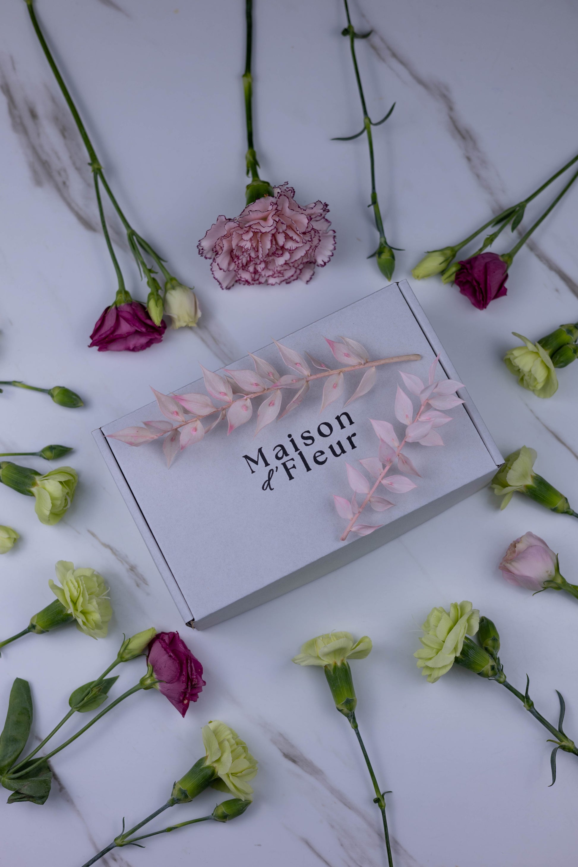 Floral arrangement with 'Maison d Fleur' box on a marble surface