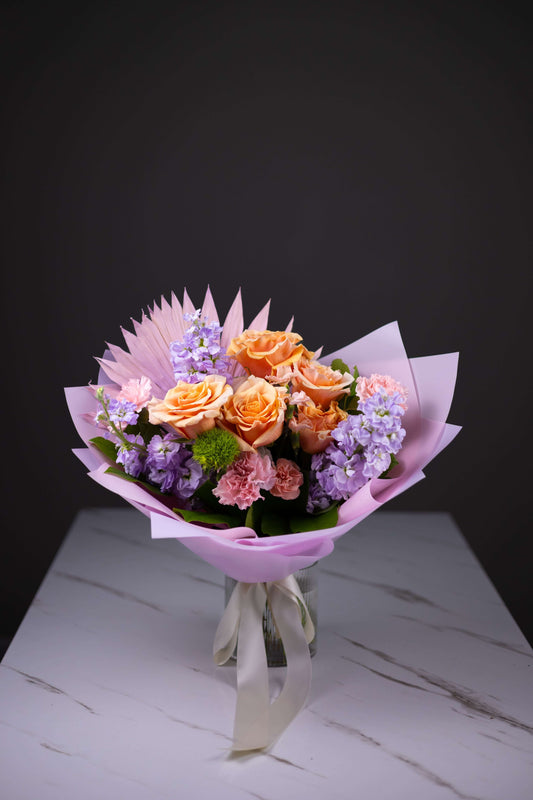 Bouquet of flowers wrapped in pink paper on a marble surface with a dark background