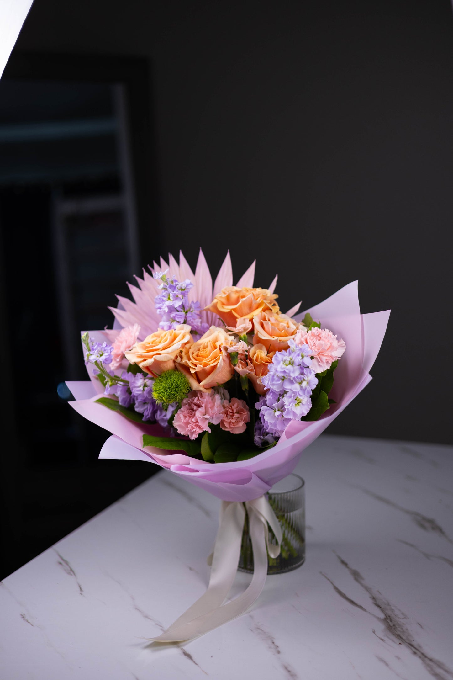 Bouquet of flowers wrapped in pink paper on a marble surface with a dark background