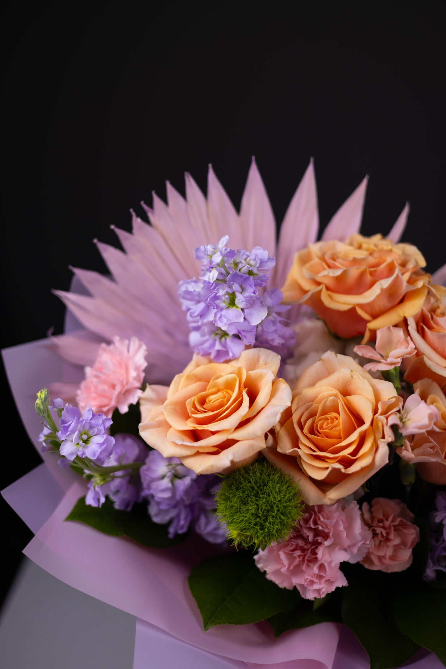 Bouquet of flowers with orange roses and pink and purple flowers on a dark background