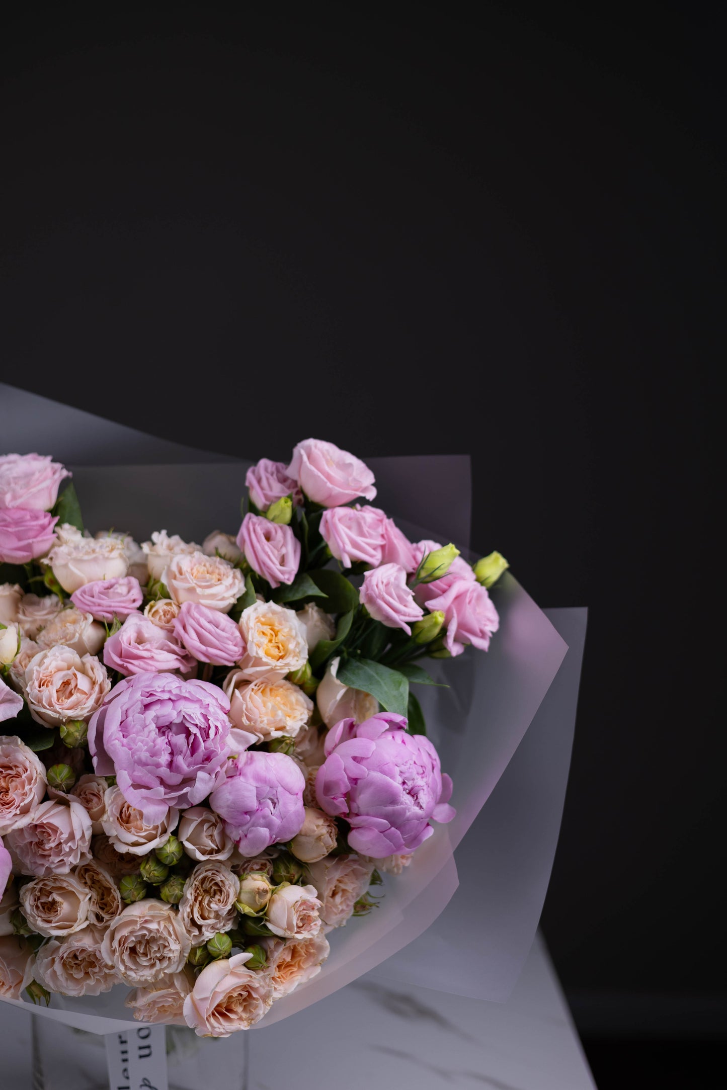 Zoomed-in section of a flower arrangement with lavender lisianthus, pale peach roses, and pink peonies.