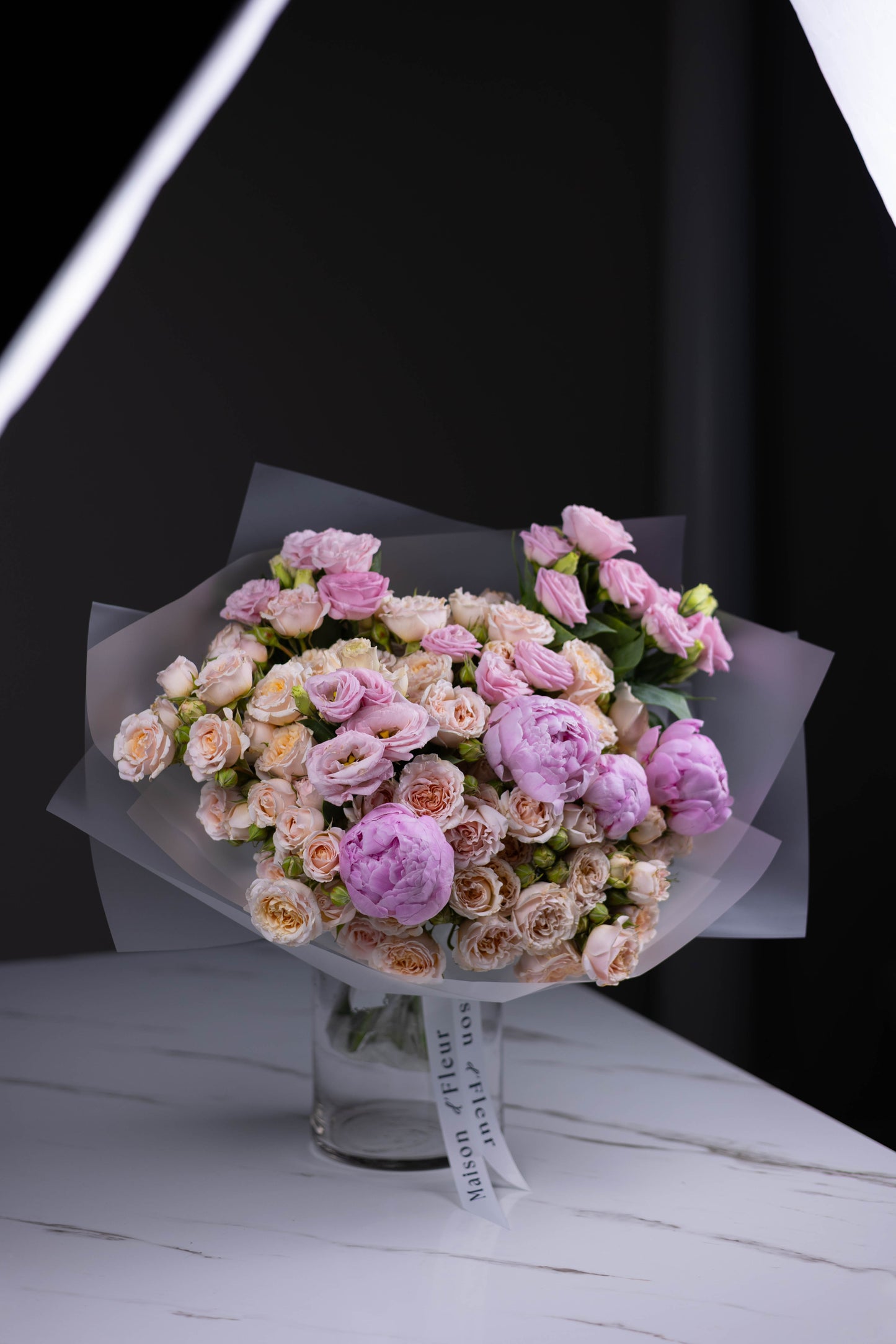 Elegant spring bouquet in soft blush tones, featuring peonies, spray roses, and lisianthus, artfully arranged in translucent wrapping.