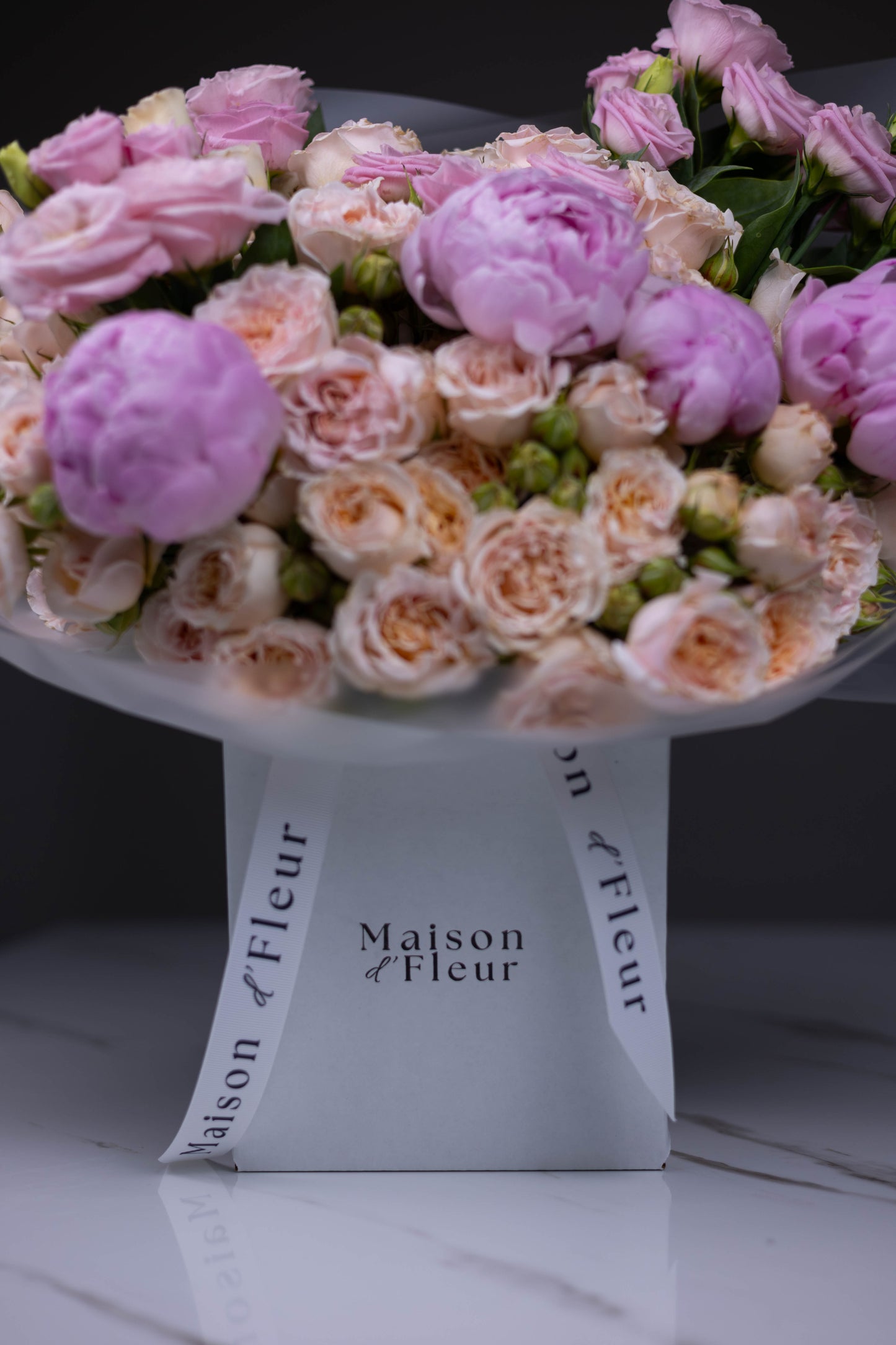 Close-up of a pastel flower bouquet featuring soft pink peonies, blush spray roses, and lisianthus, arranged in a white Maison d’Fleur branded gift box with elegant white ribbon.
