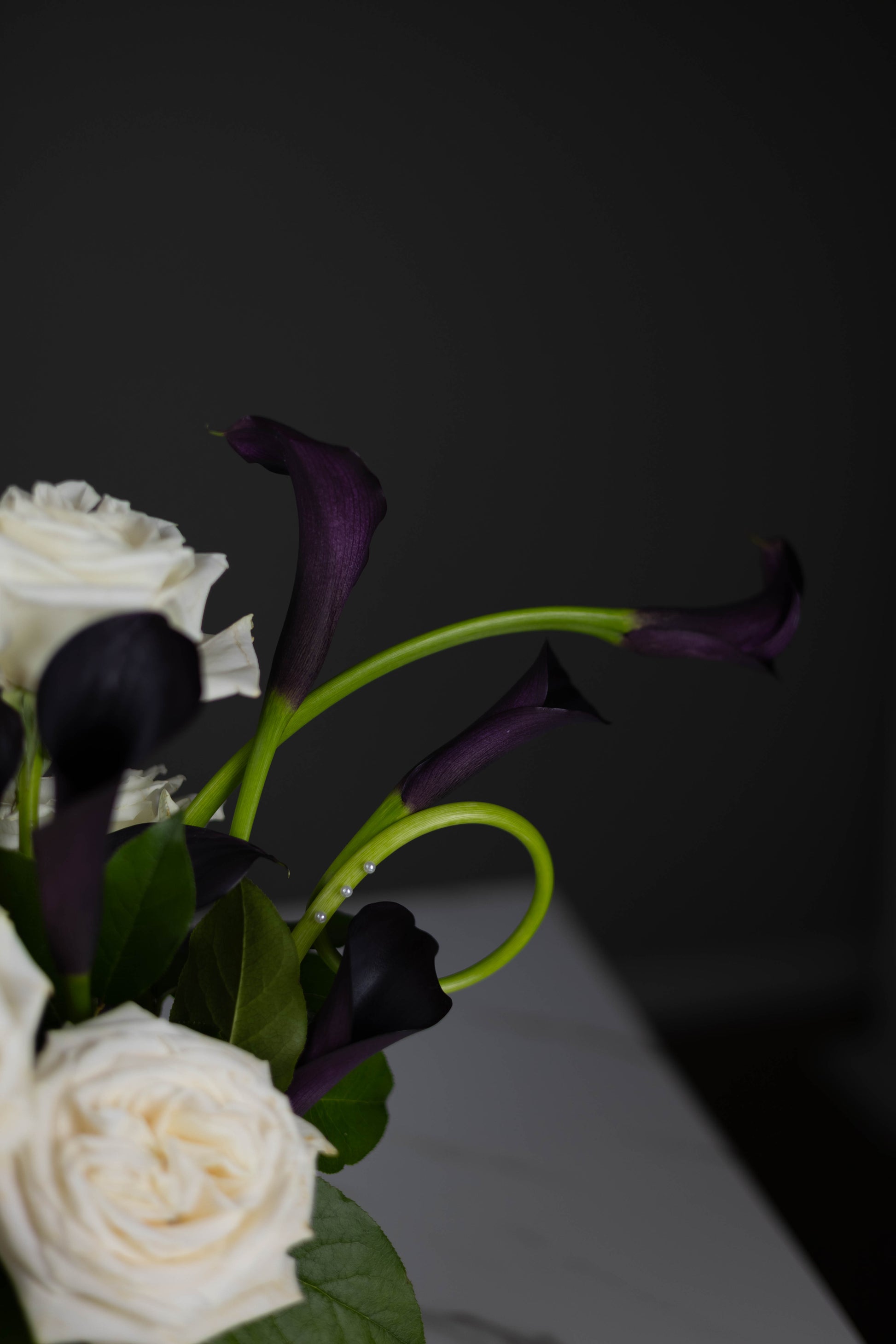 Close-up of black calla lilies with elegant curved green stems in a designer arrangement