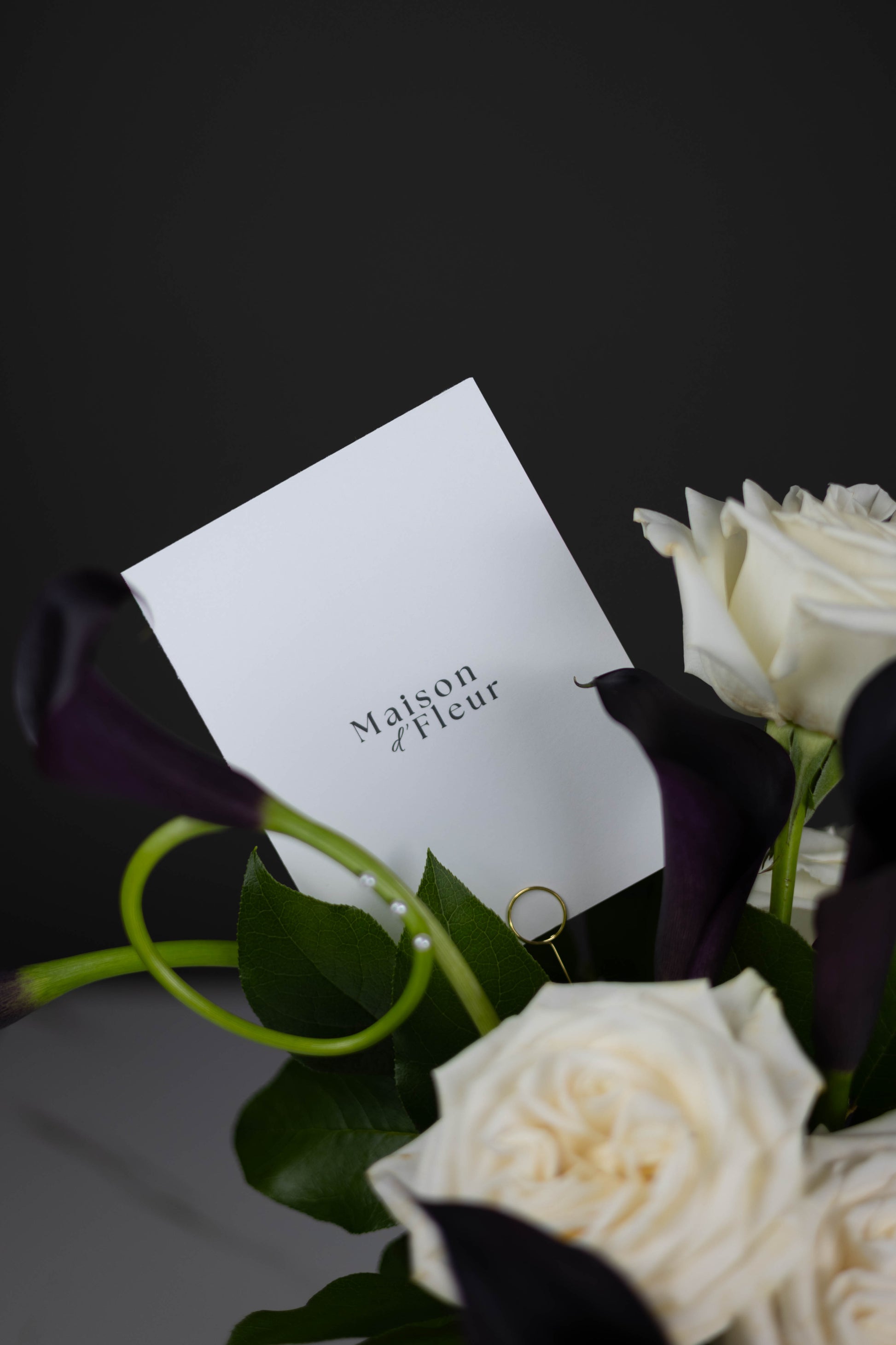 Luxury floral card by Maison d’Fleur nestled among white roses and deep purple calla lilies