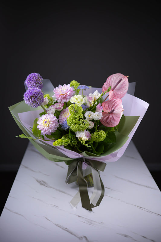 Front view of the wrapped pastel bouquet with anthuriums, dahlias, and alliums