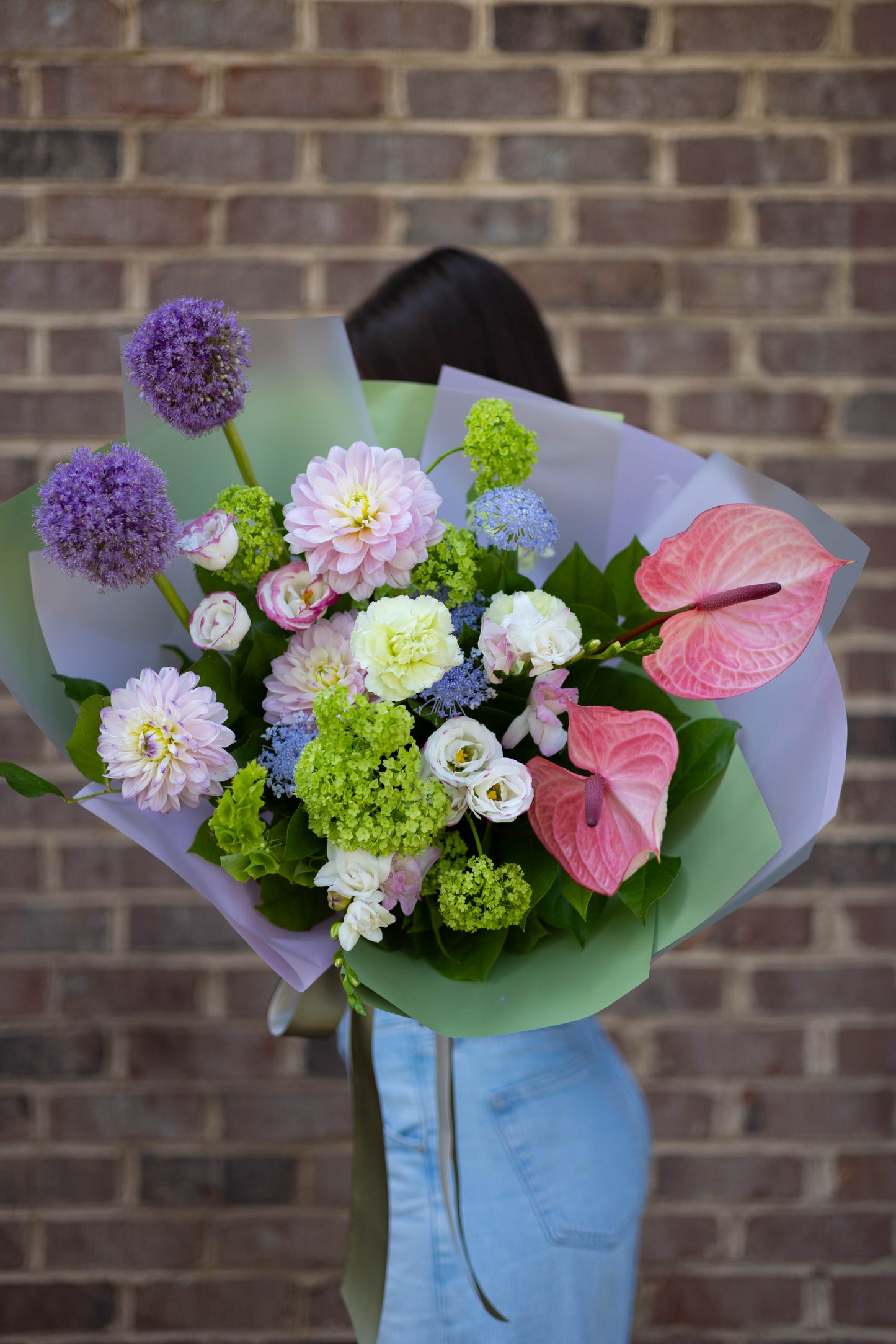 Lifestyle shot of a person holding the pastel bouquet against a brick wall