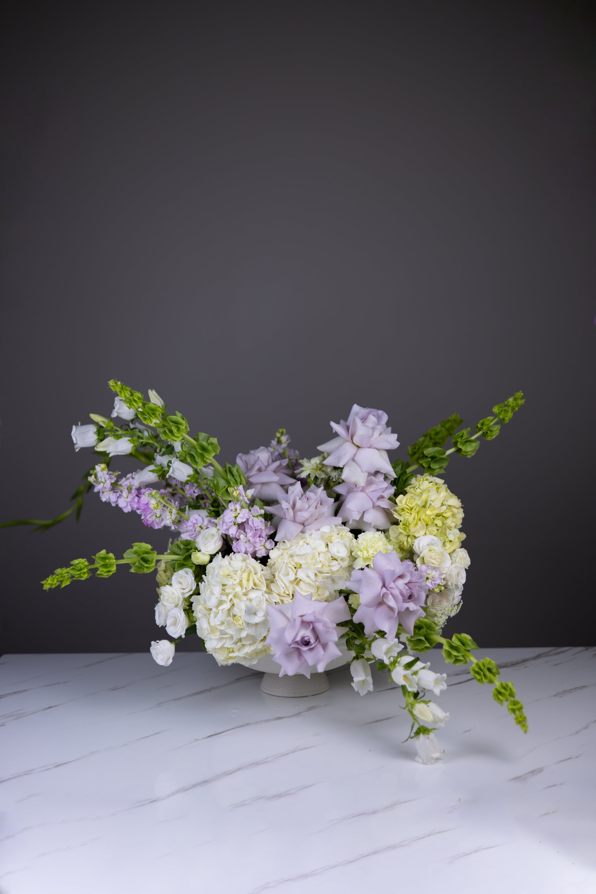Floral arrangement in a glass vase on a white surface with a dark gray background