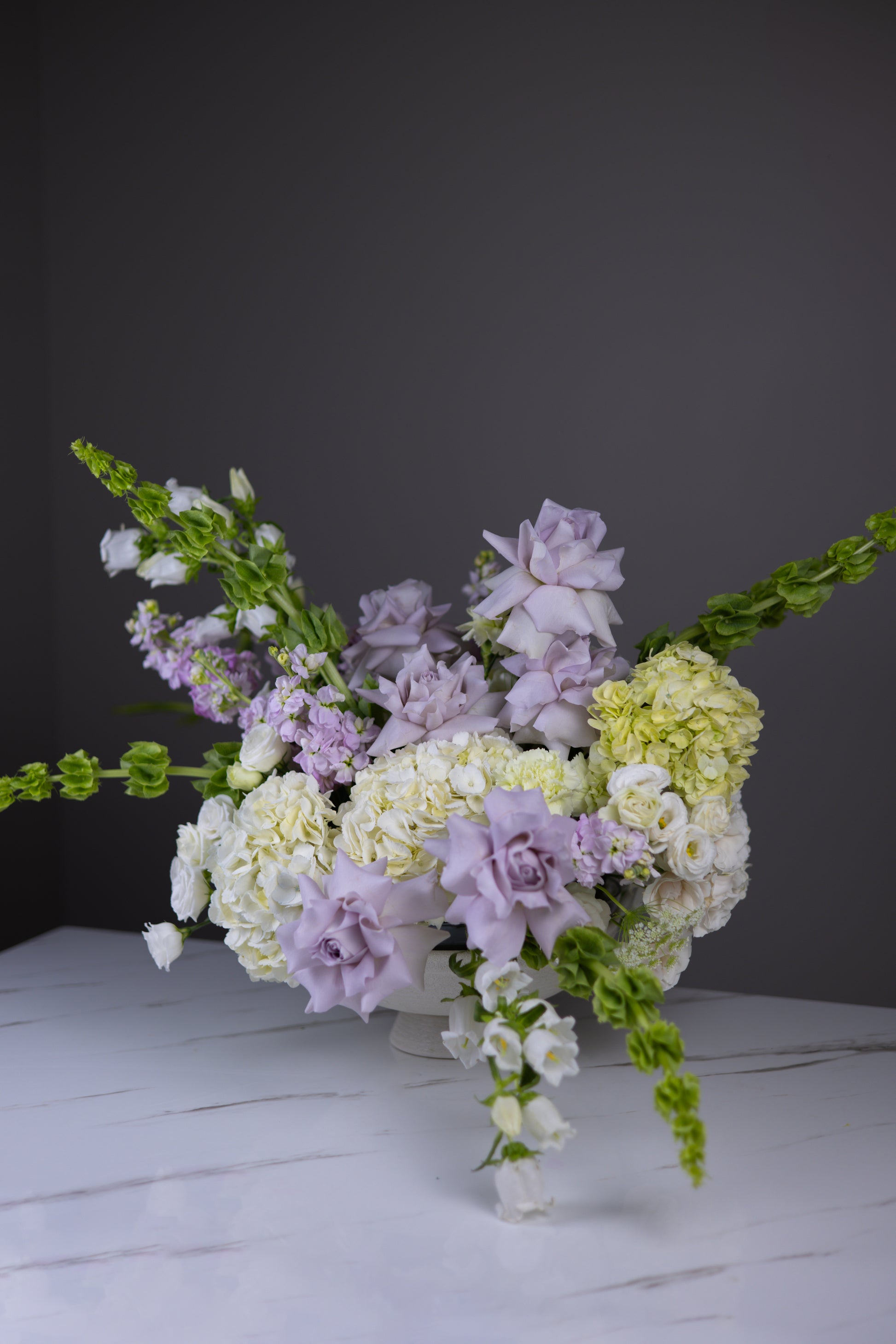 Side view of an airy lavender and ivory floral centerpiece with lush blooms and trailing greens.