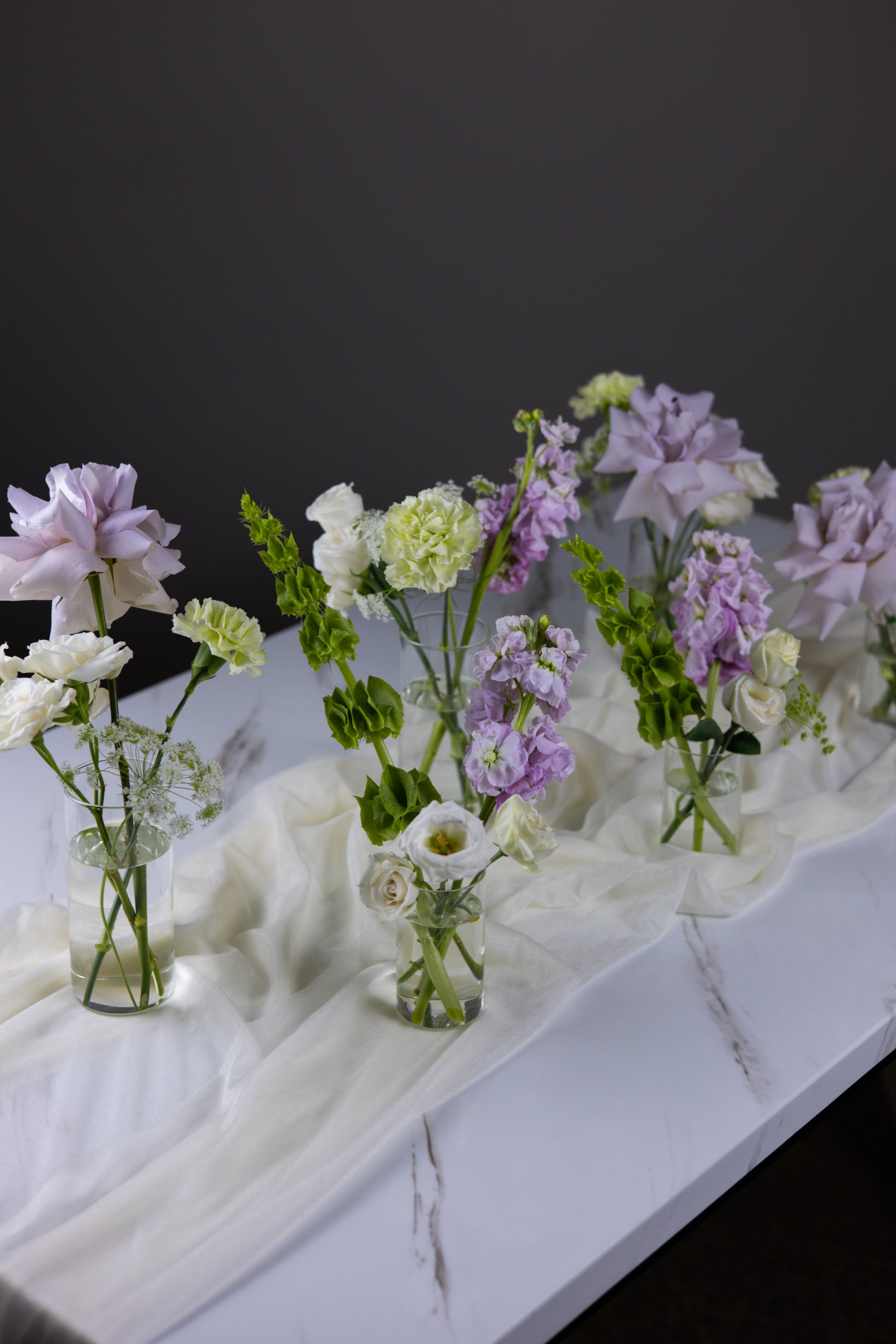 Row of small floral arrangements on a marble surface with a dark background