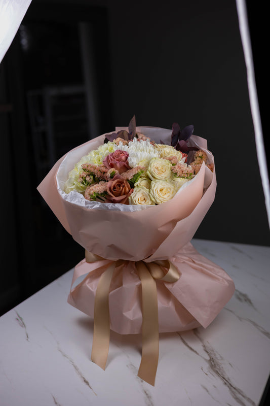 Bouquet of flowers wrapped in pink paper with a bow on a marble surface.