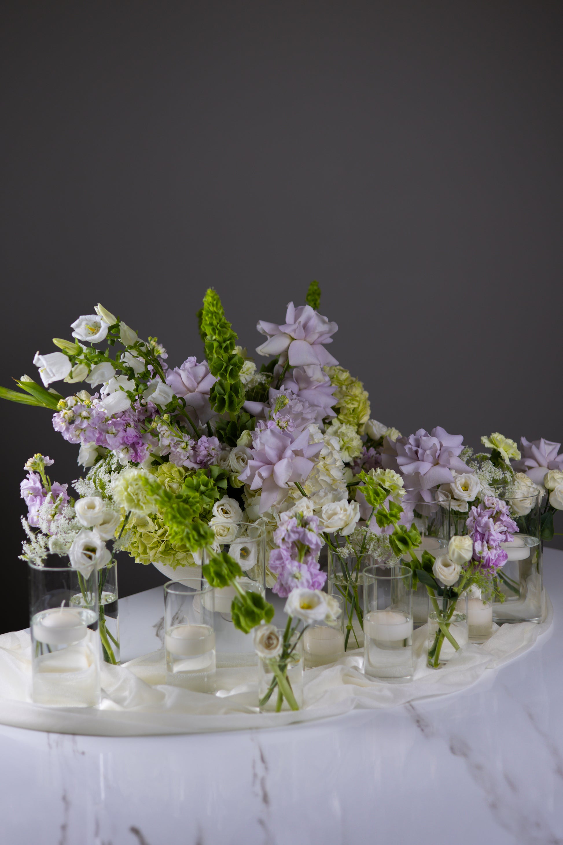 Decorative floral arrangement with small vases on a marble surface against a dark background