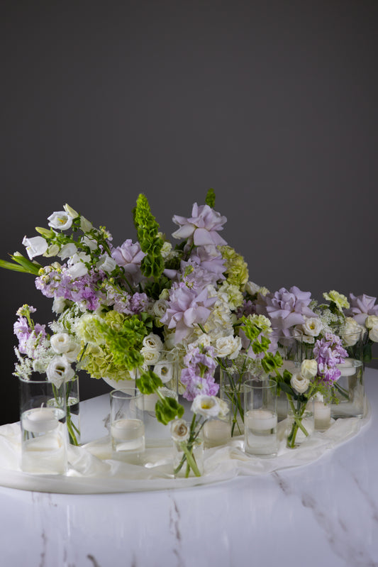 Decorative floral arrangement with small vases on a marble surface against a dark background