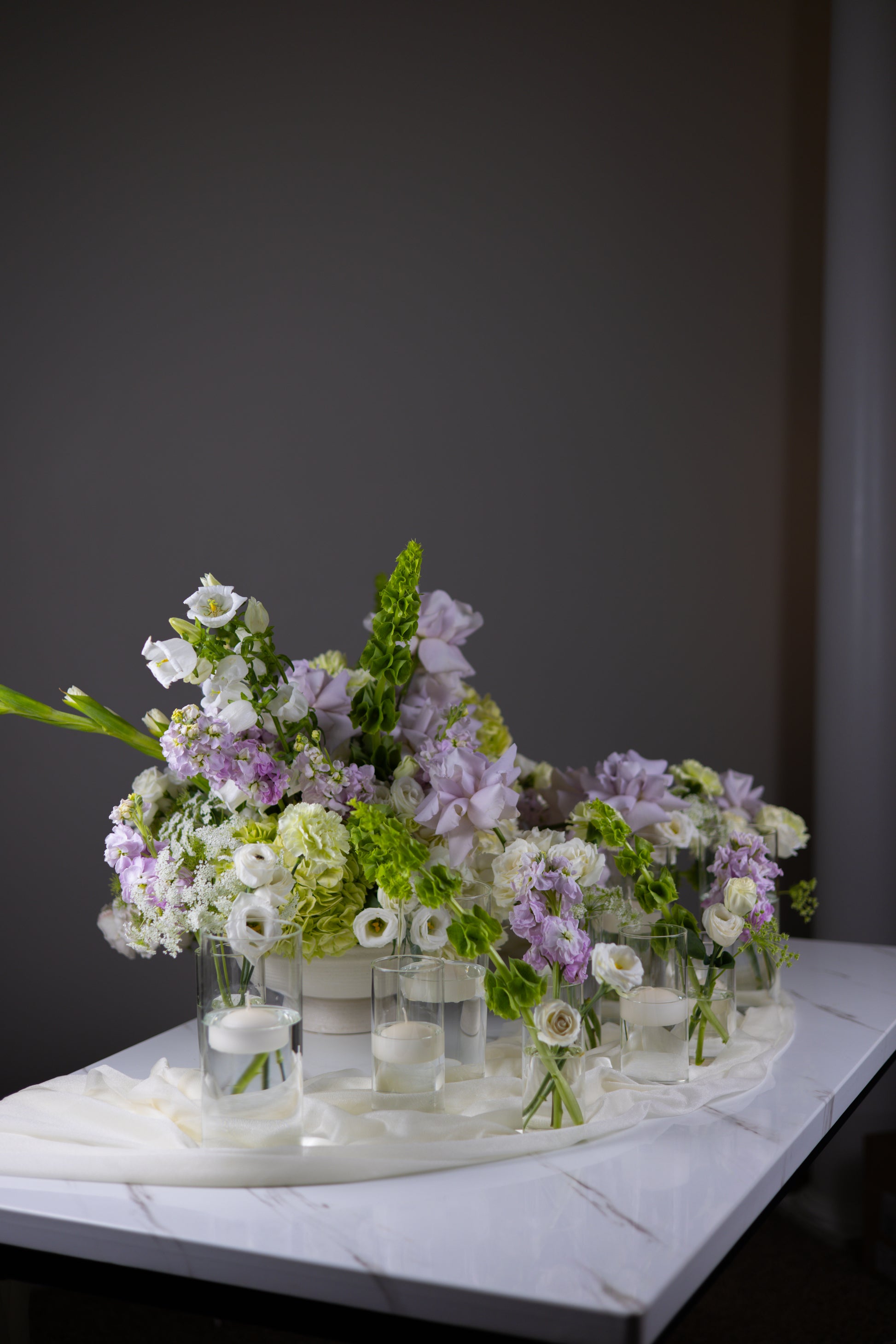 Bouquets of flowers in clear vases on a marble surface with a dark background