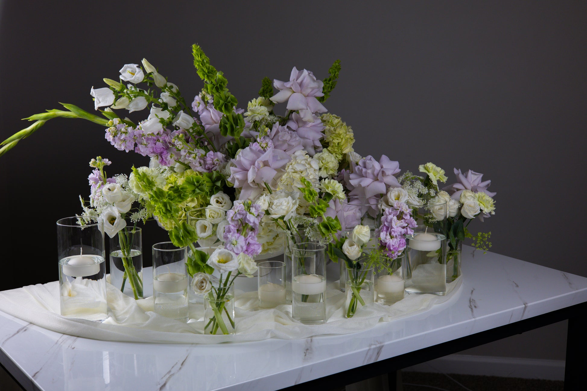 Floral arrangement with small vases on a marble surface against a dark background