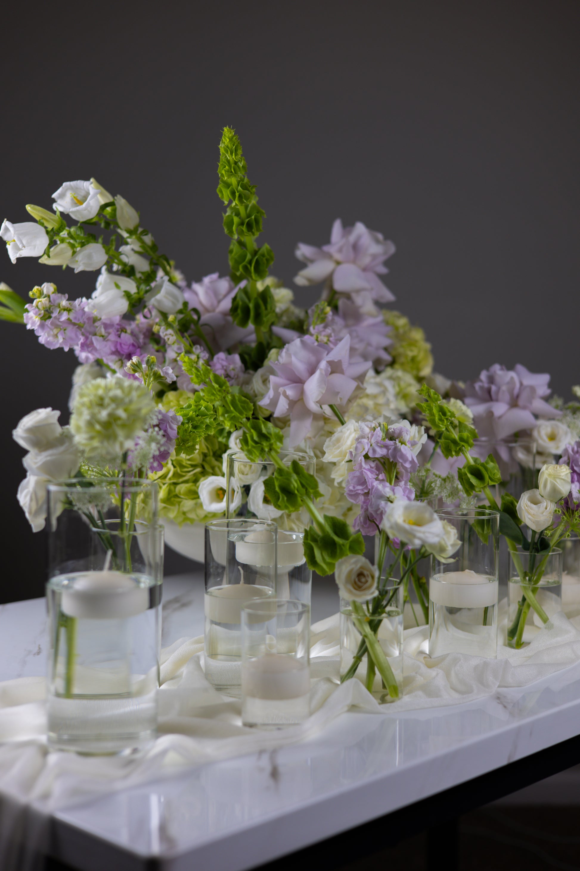 Bouquets of flowers in clear vases on a white tablecloth with a dark background