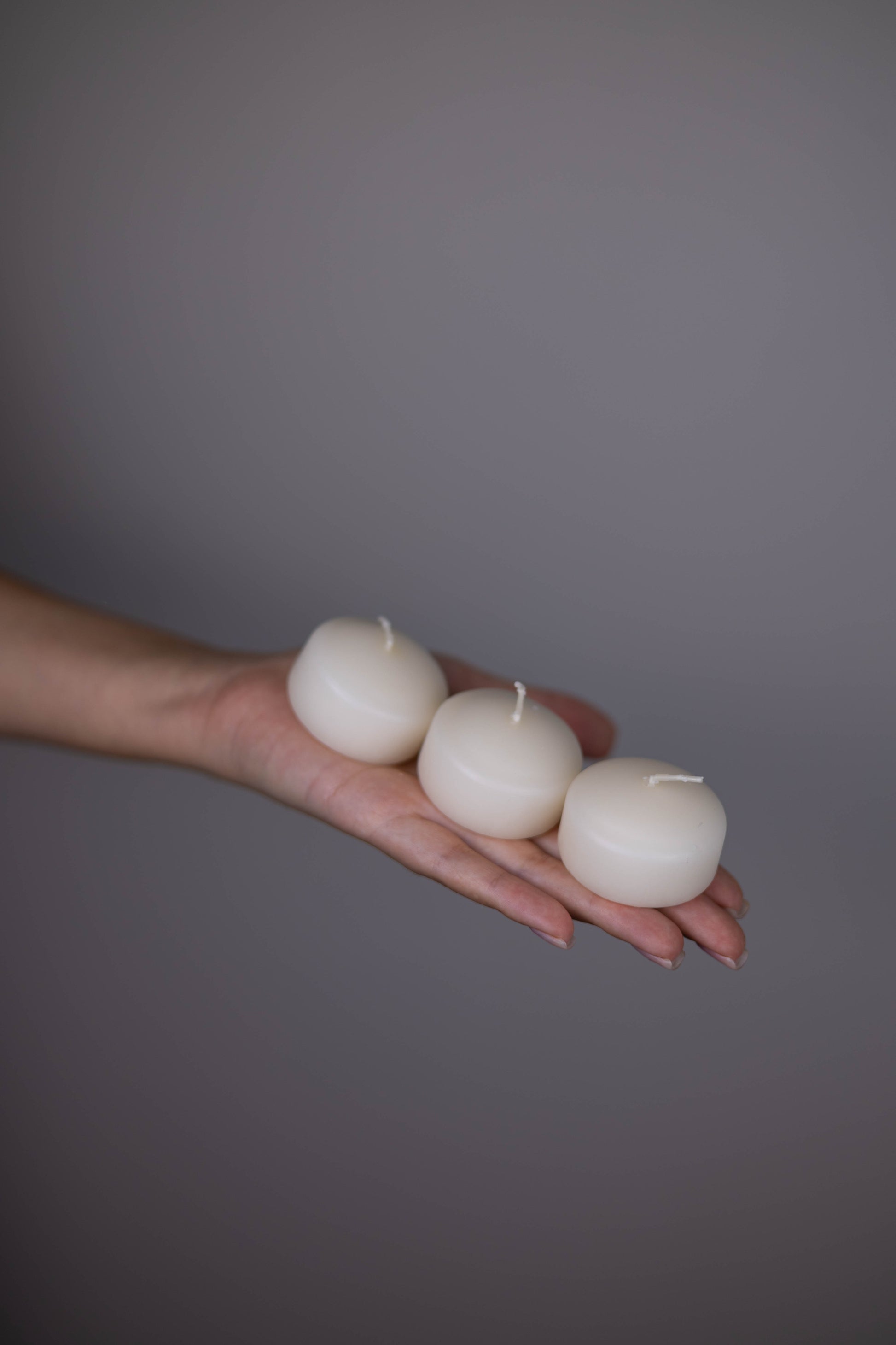 Hand holding three white candles against a gray background