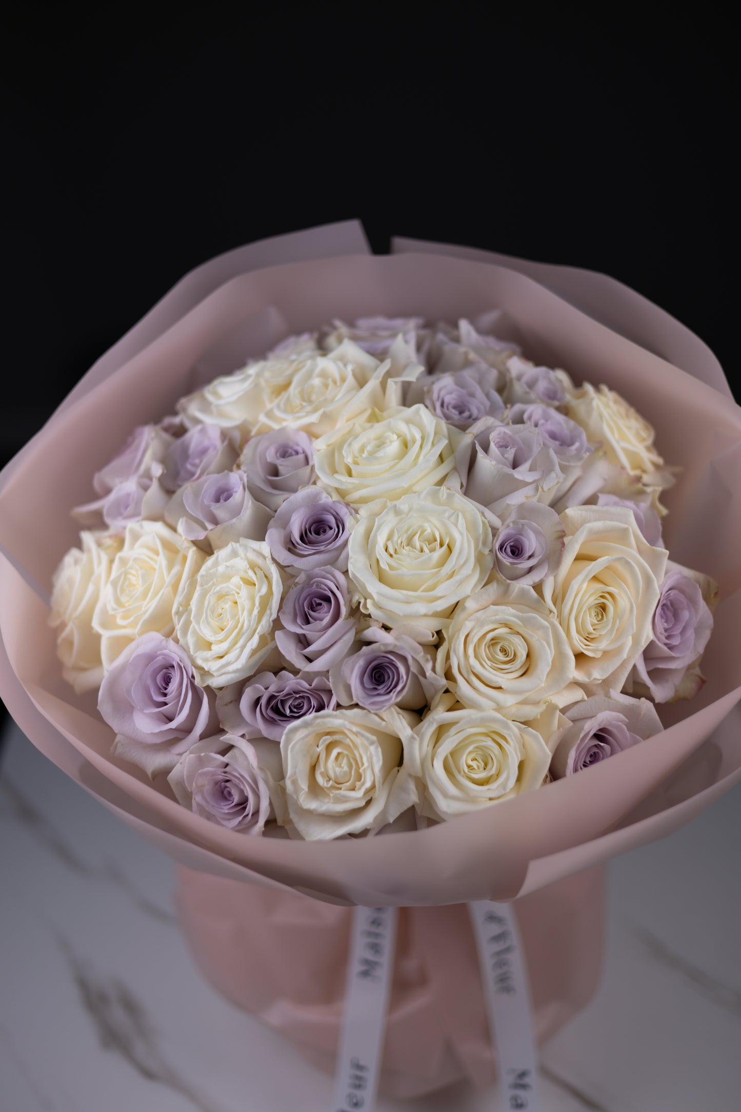 Close-up view of a pastel bouquet of ivory and lavender roses in blush wrapping.