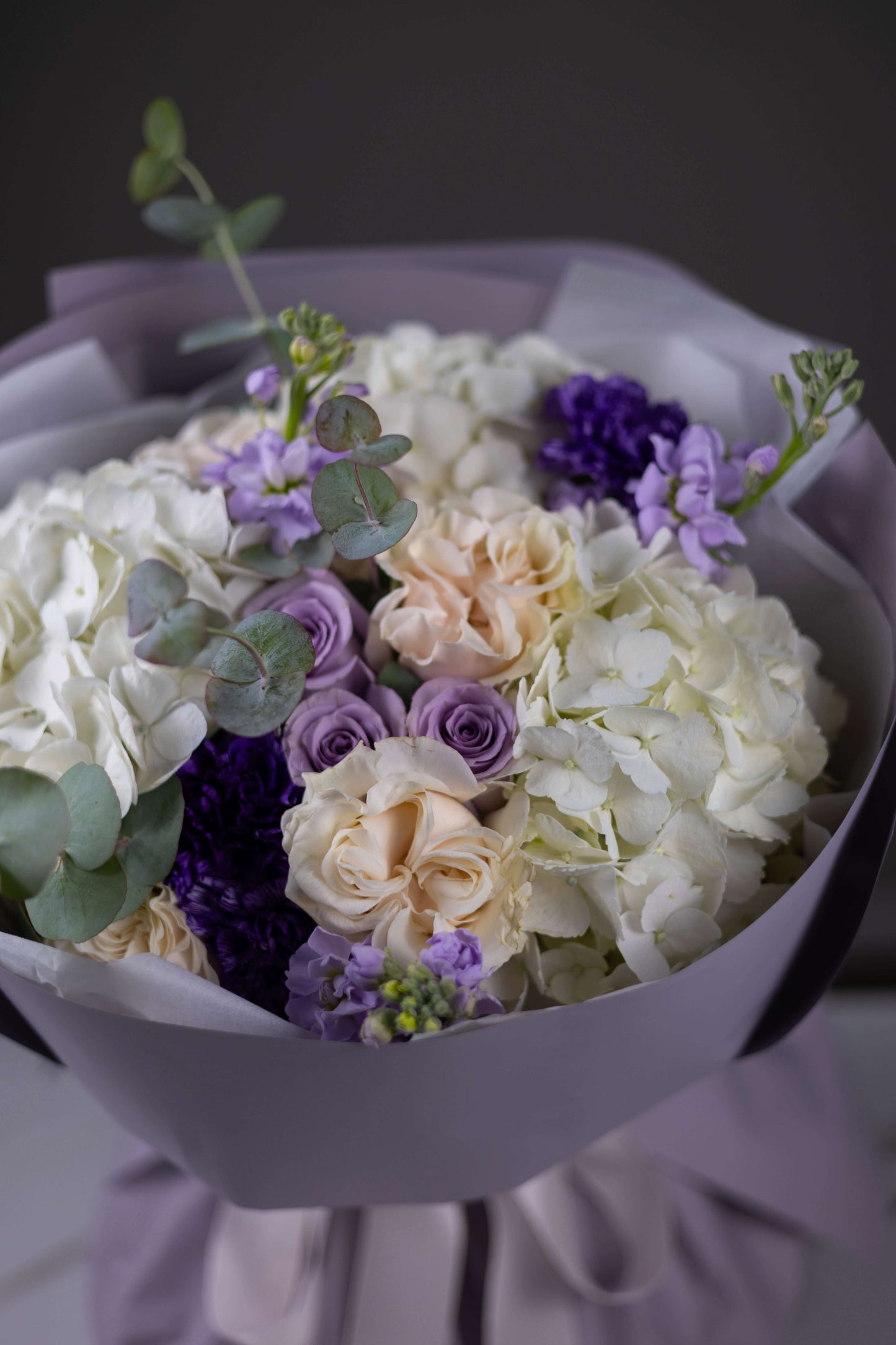 Bouquet of flowers with white, purple, and beige colors in a gray wrap.