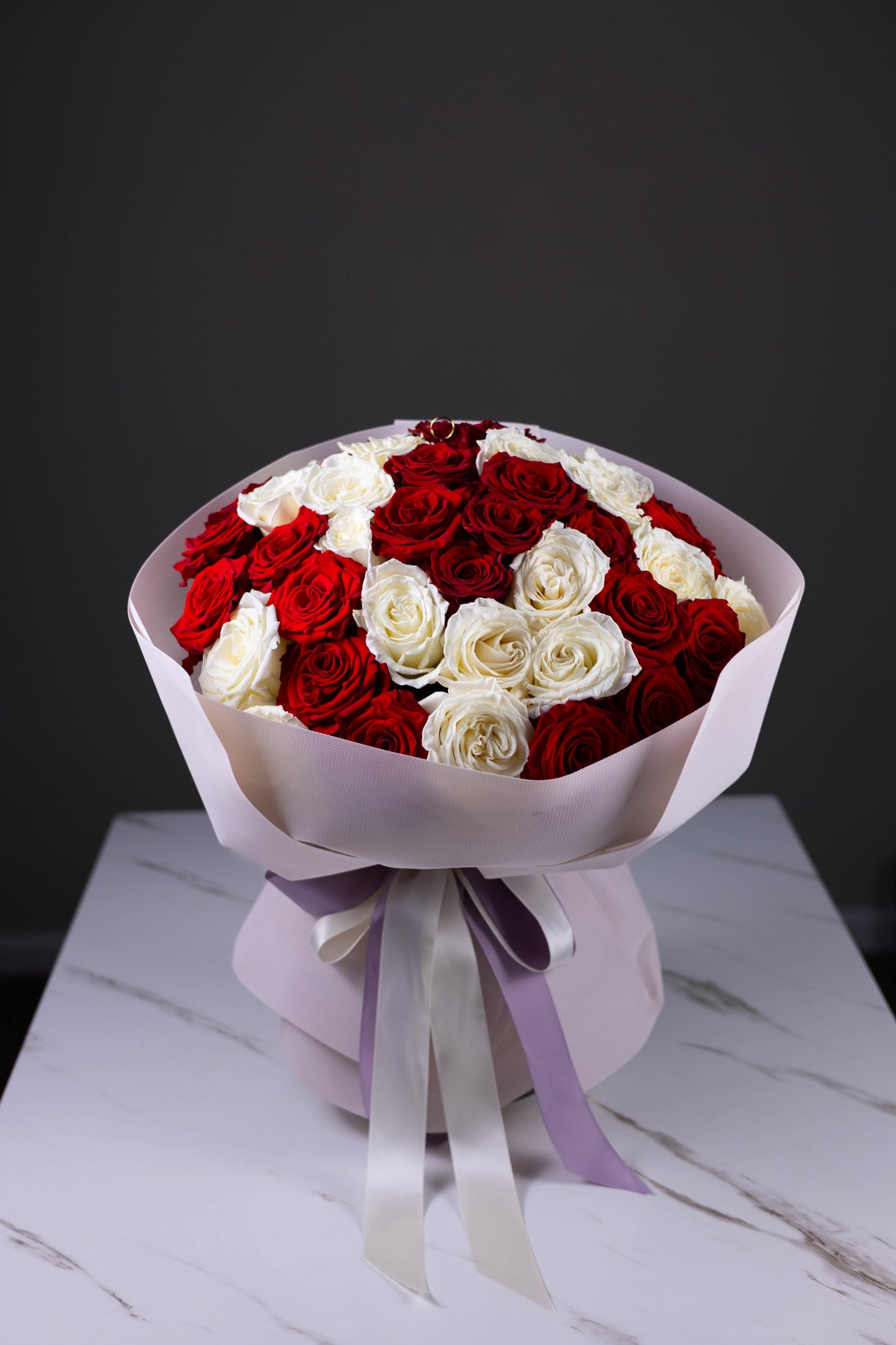 Bouquet of red and white roses wrapped in paper with a ribbon on a marble surface.