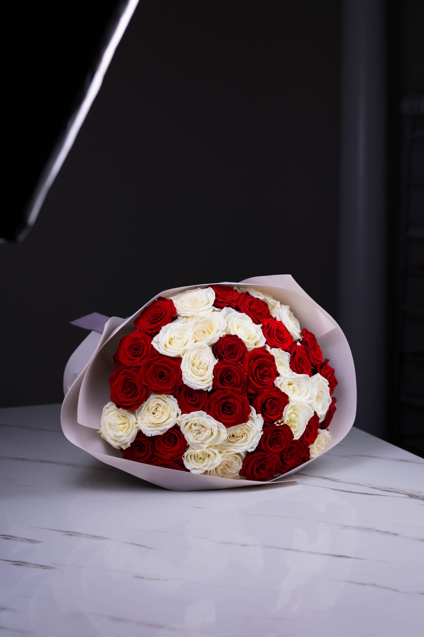 Front view of a large bouquet with red and white roses arranged in a checkerboard pattern, wrapped in matte blush paper