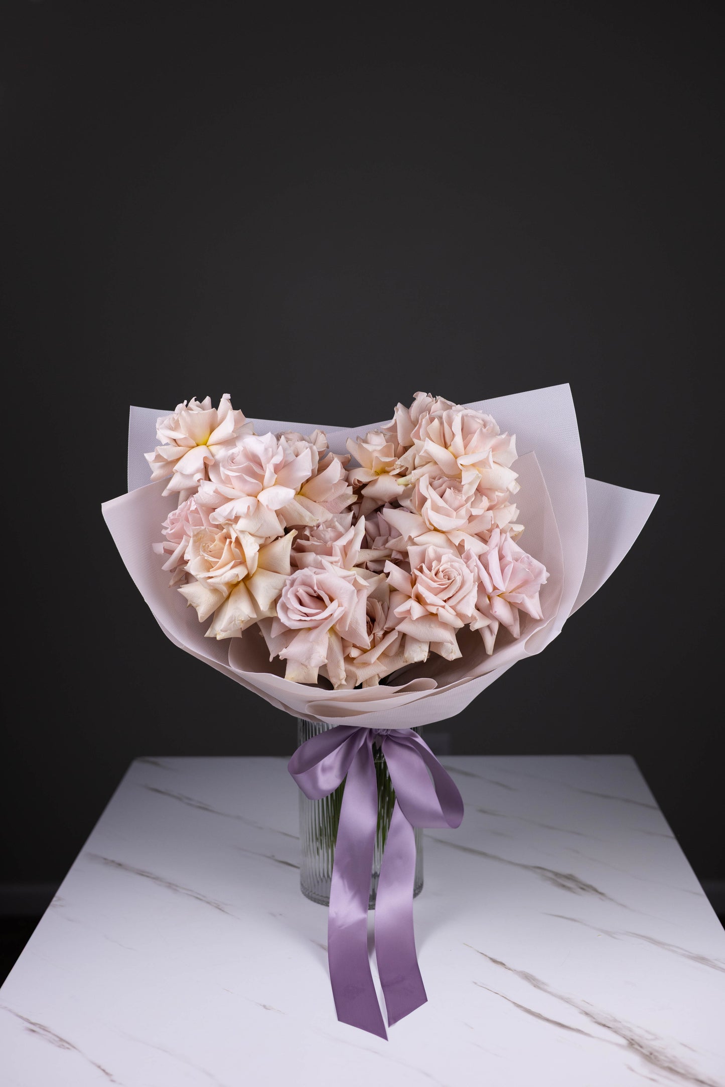 Bouquet of pink flowers with a purple ribbon on a marble surface against a black background
