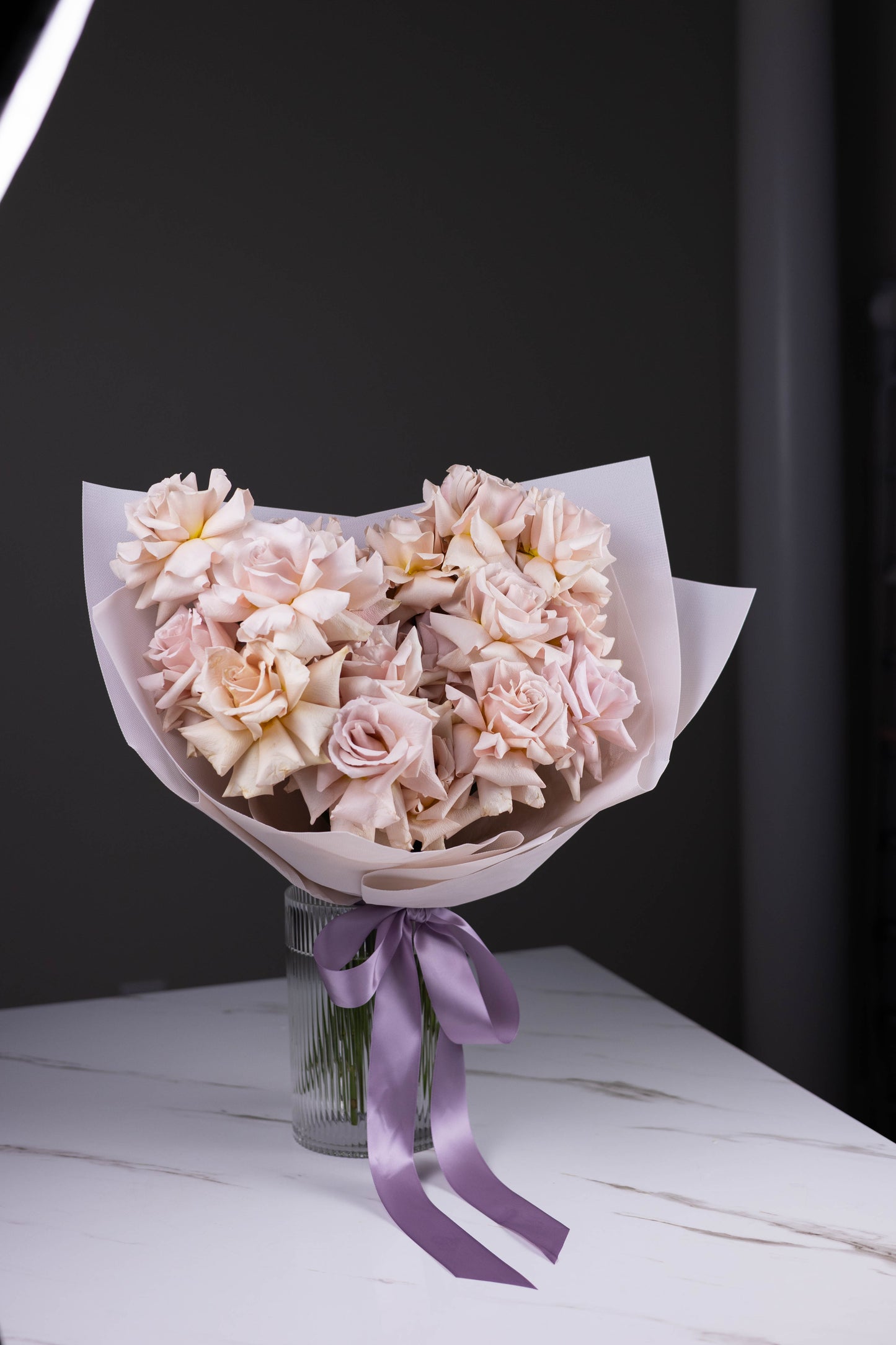 Side angle of pastel rose bouquet with lavender ribbon, showing elegant wrapping and vase