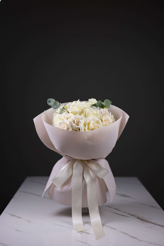 Bouquet of white flowers wrapped in pink paper with a white ribbon on a dark background