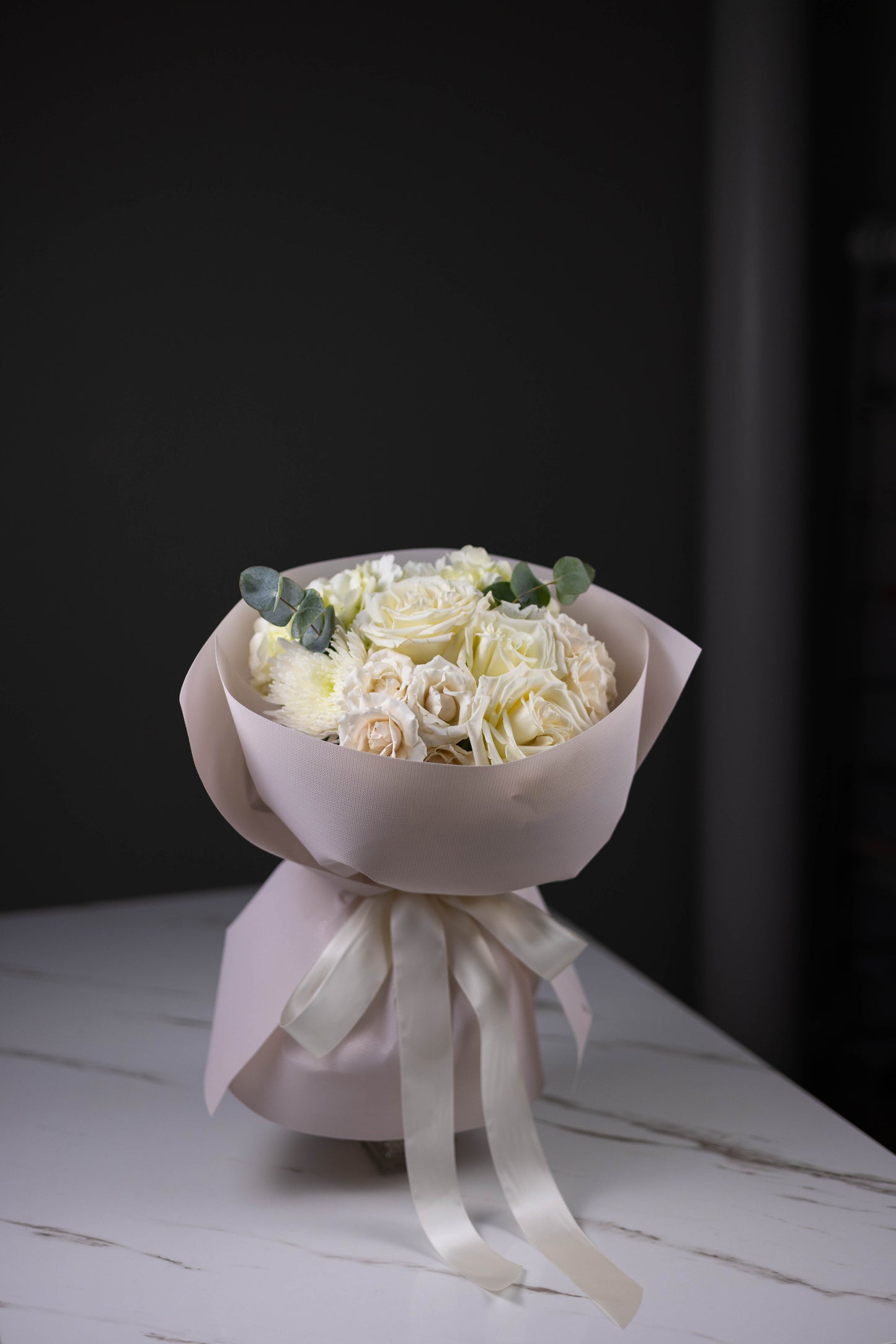 Bouquet of white flowers wrapped in pink paper with a white ribbon on a dark background