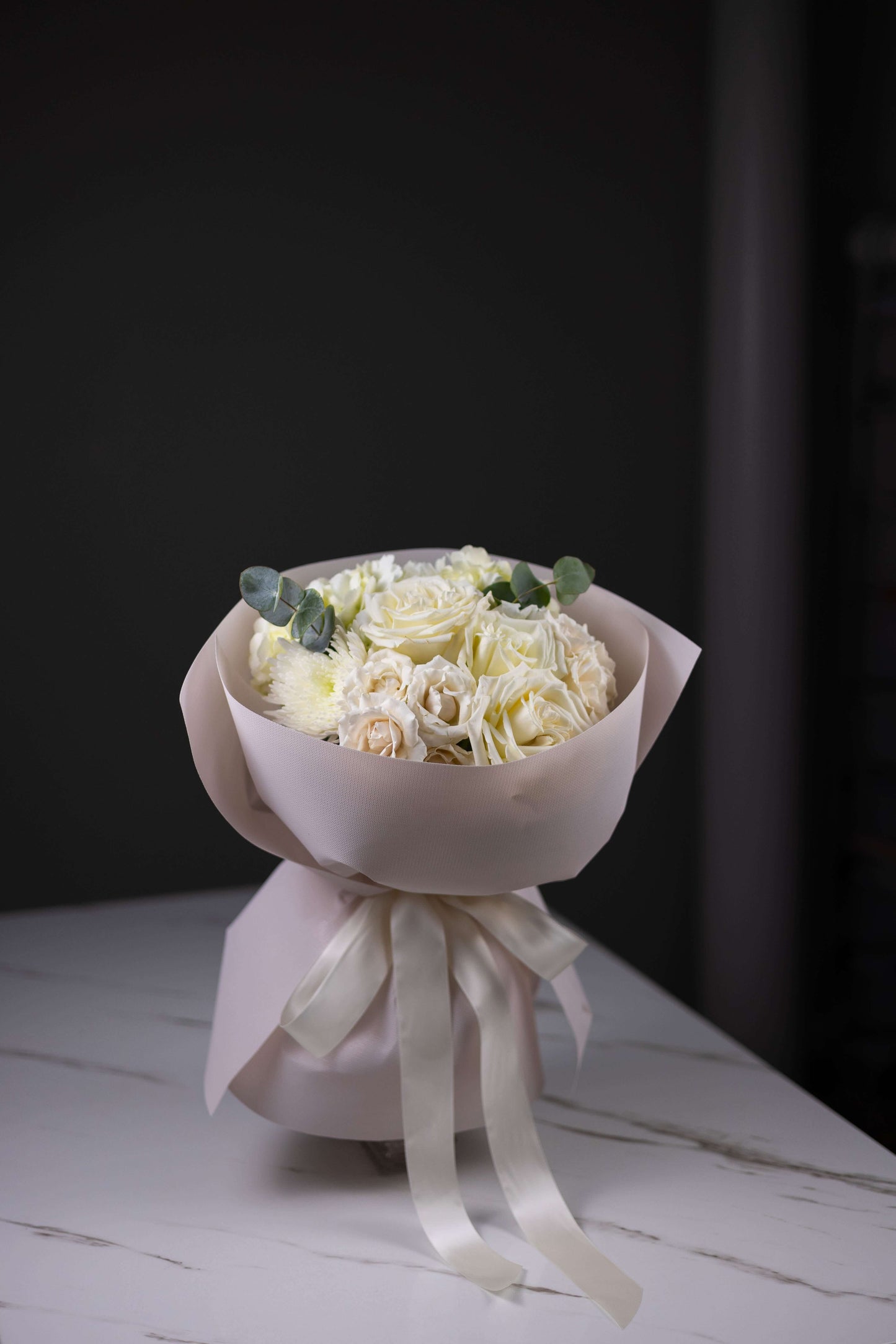 Bouquet of white flowers wrapped in pink paper with a white ribbon on a dark background