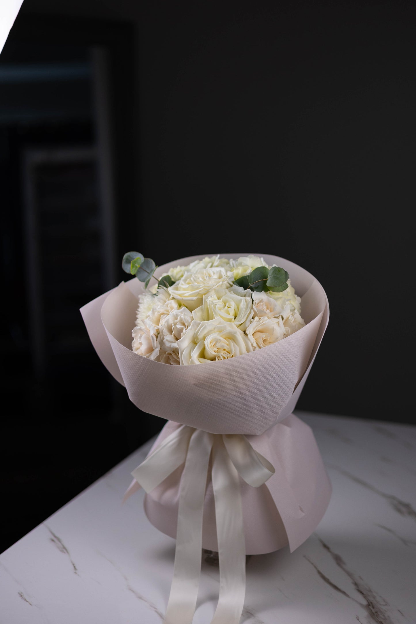 Bouquet of white flowers wrapped in paper with a ribbon on a dark background