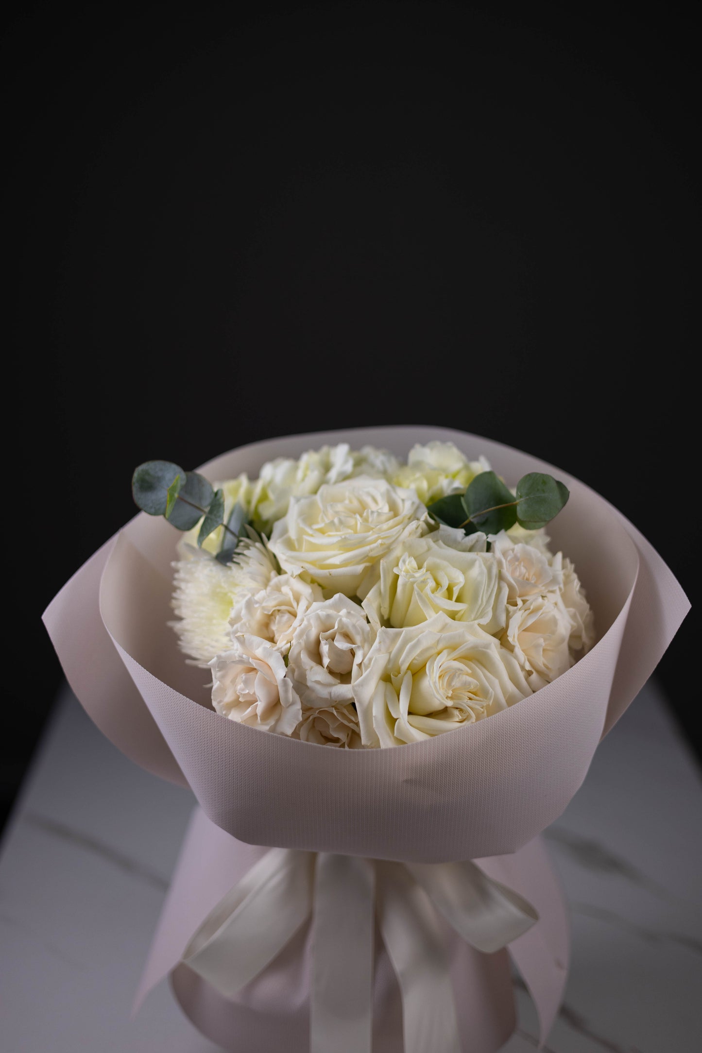 Bouquet of white roses wrapped in pink paper on a dark background