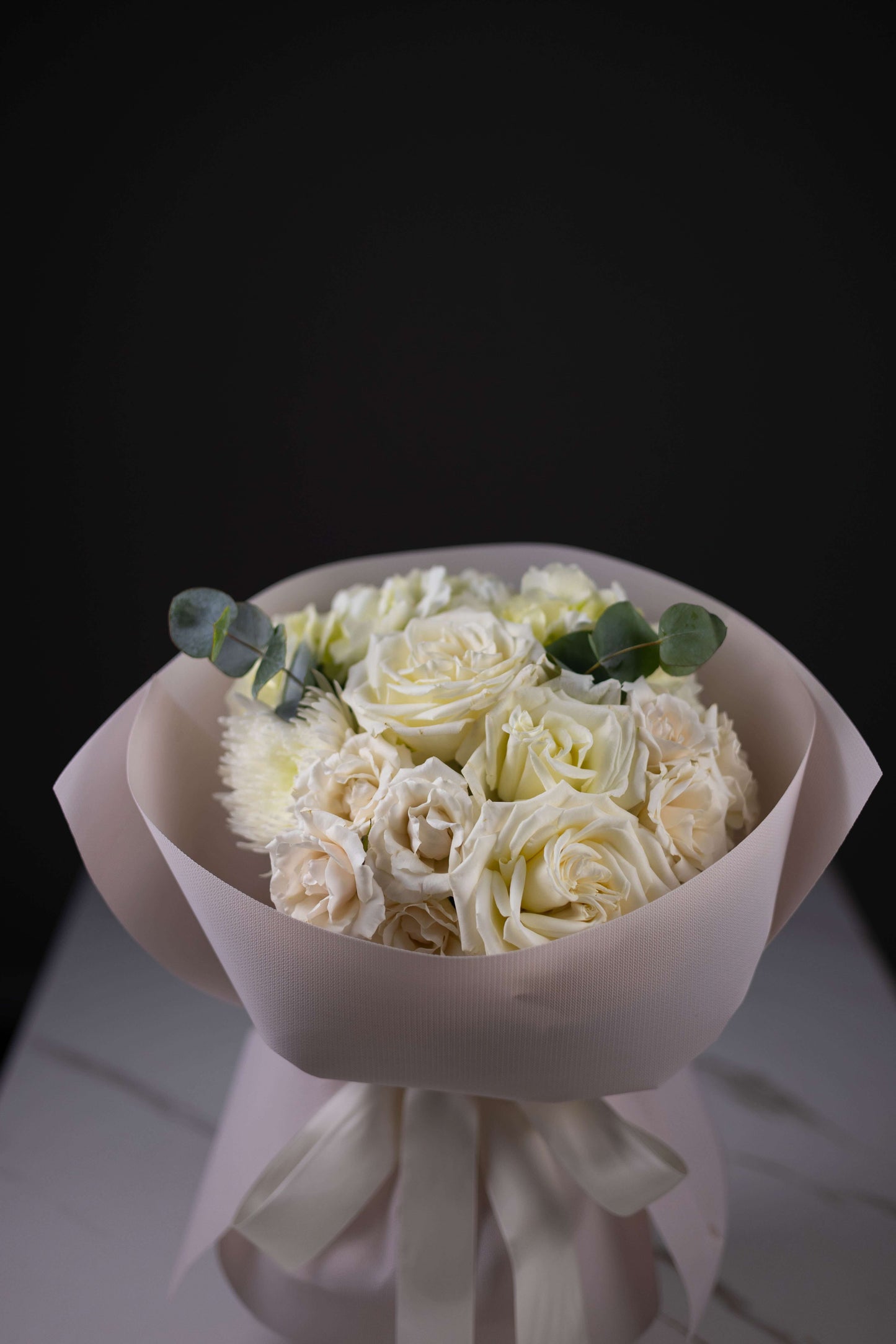 Bouquet of white roses wrapped in pink paper on a dark background