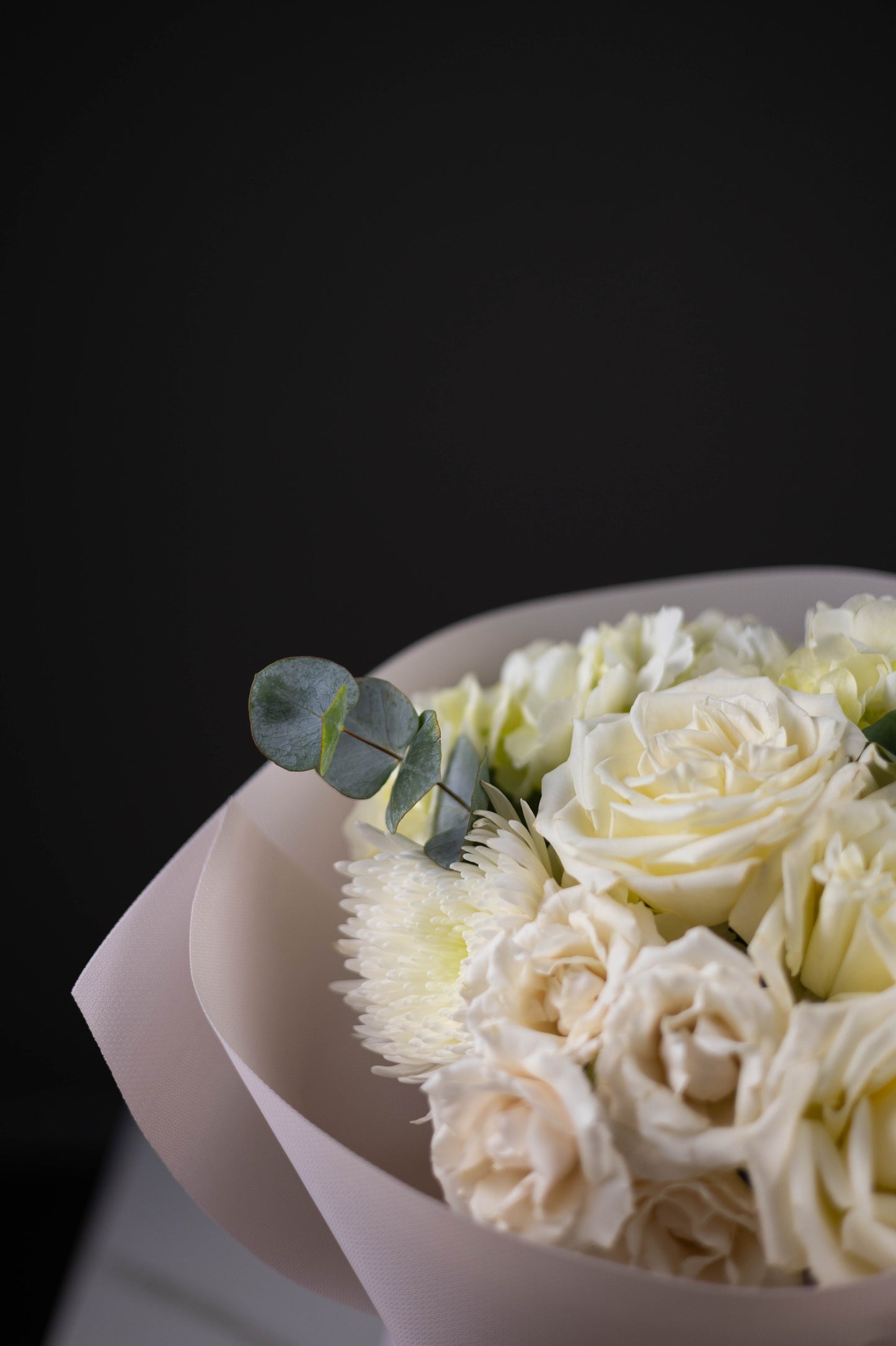 Bouquet of white roses with eucalyptus in a clear container against a dark background