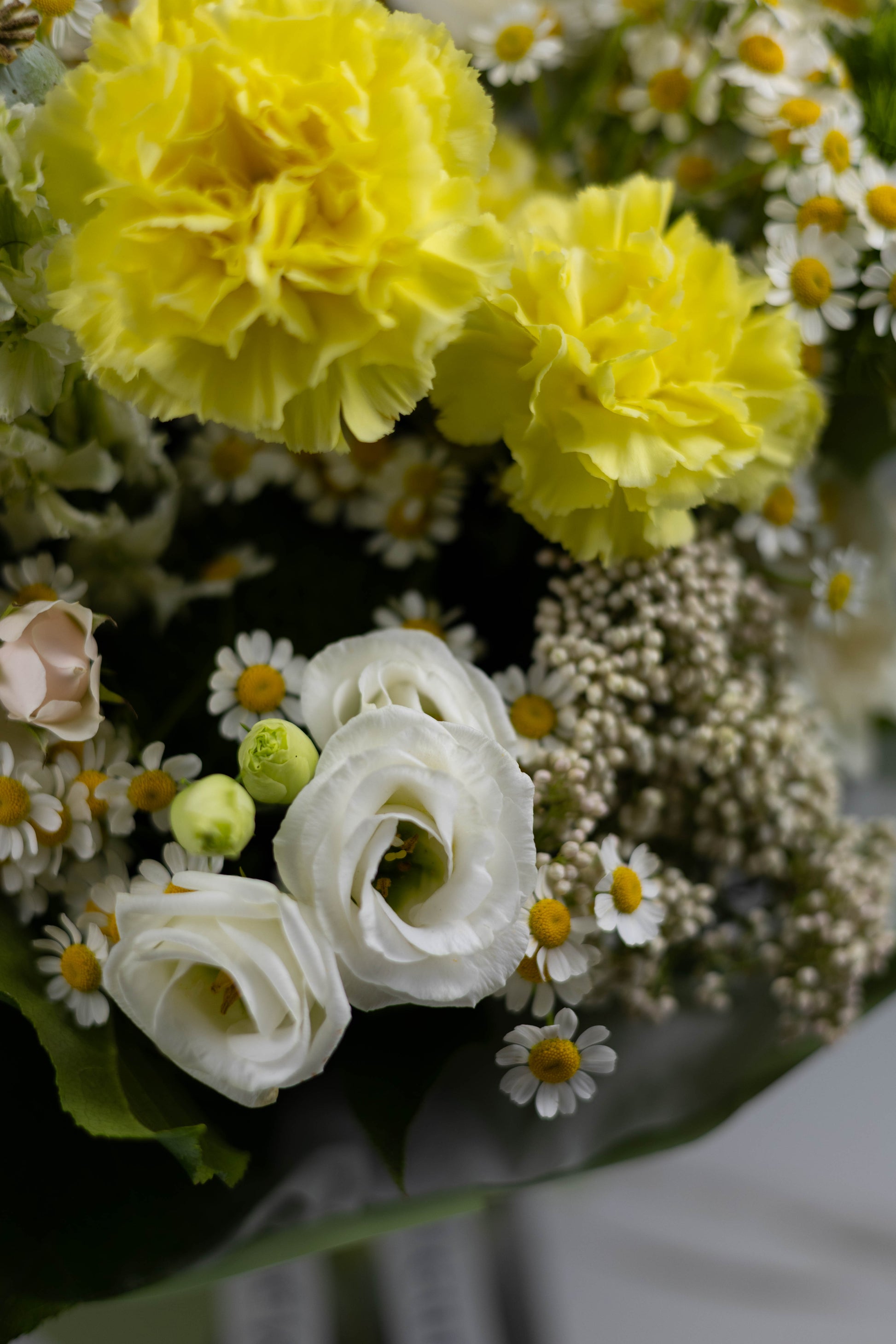Detailed view of yellow carnations and crisp white lisianthus surrounded by clusters of chamomile, creating a joyful and textural floral arrangement.