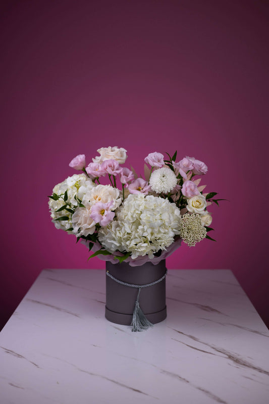 Bouquet of flowers in a gray vase on a white surface with a pink background