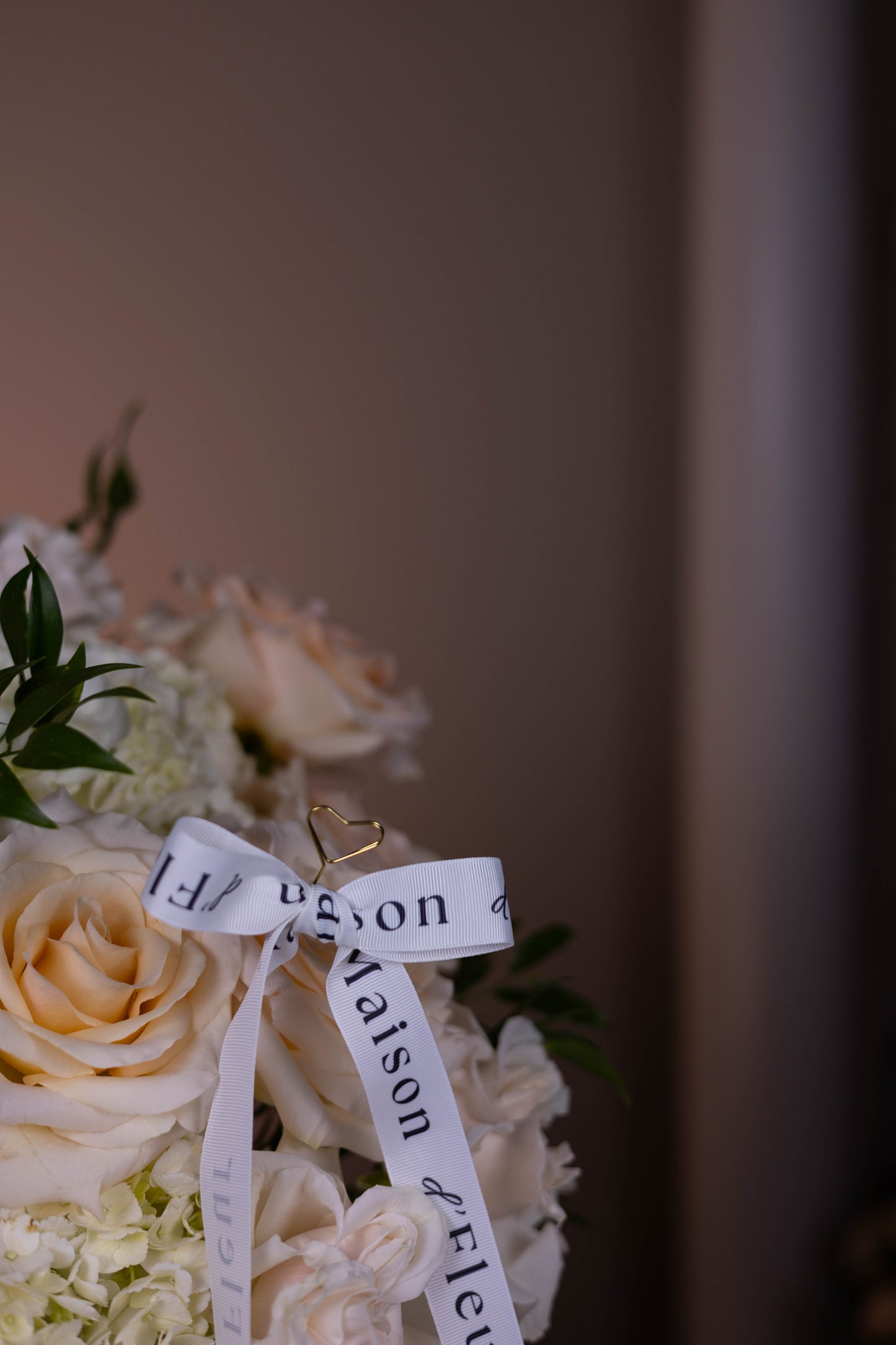 Floral arrangement with a ribbon and ring, featuring the brand 'Maison d'Fleur'.