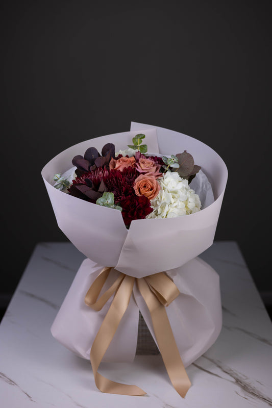 Luxurious fall flower arrangement with warm-toned roses and burgundy florals in signature wrapping – Maison d’Fleur florist Charlotte North Carolina